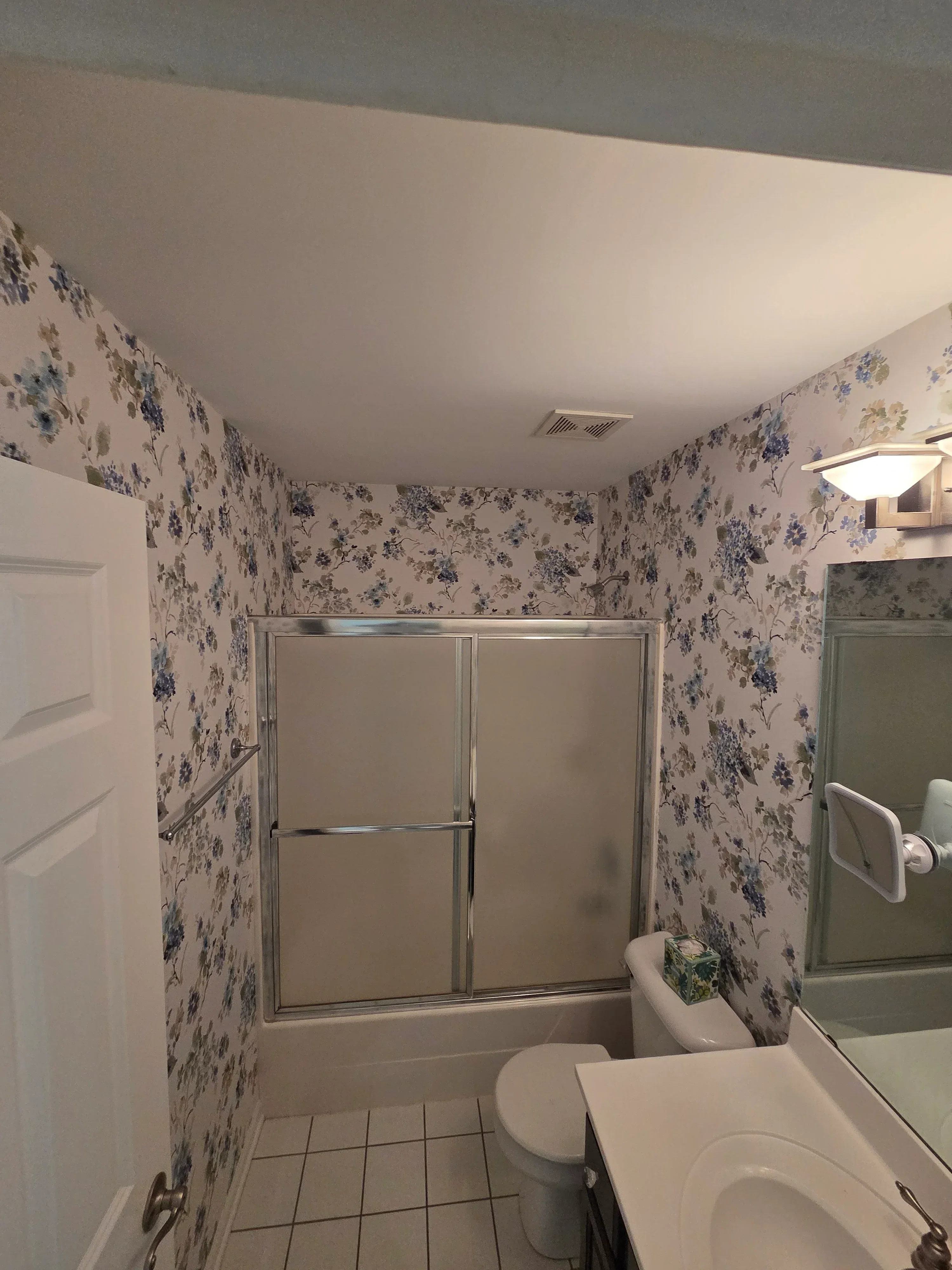 Bathroom with blue floral wallpaper on walls and ceiling, framed shower enclosure, white fixtures