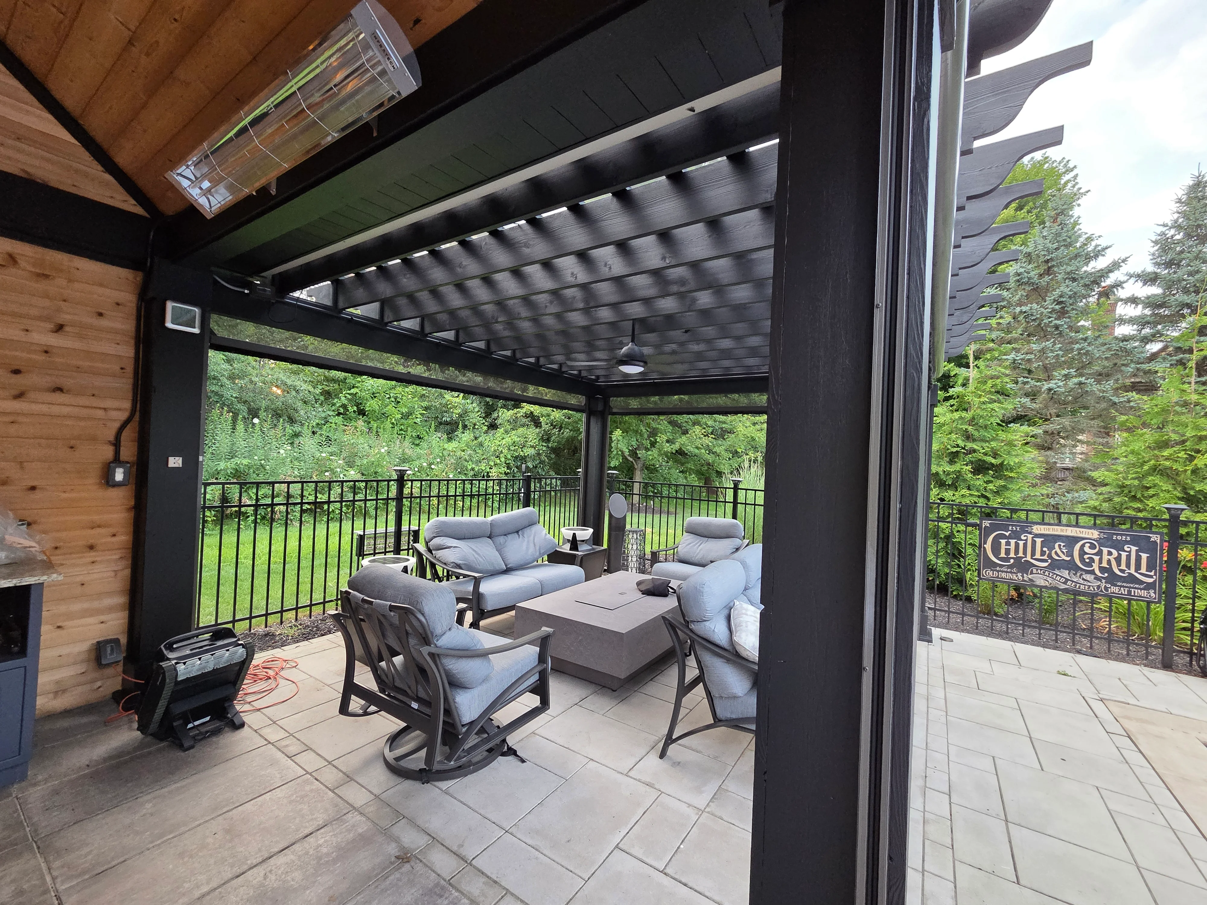 Black painted pergola with shade system and cedar siding on residential patio