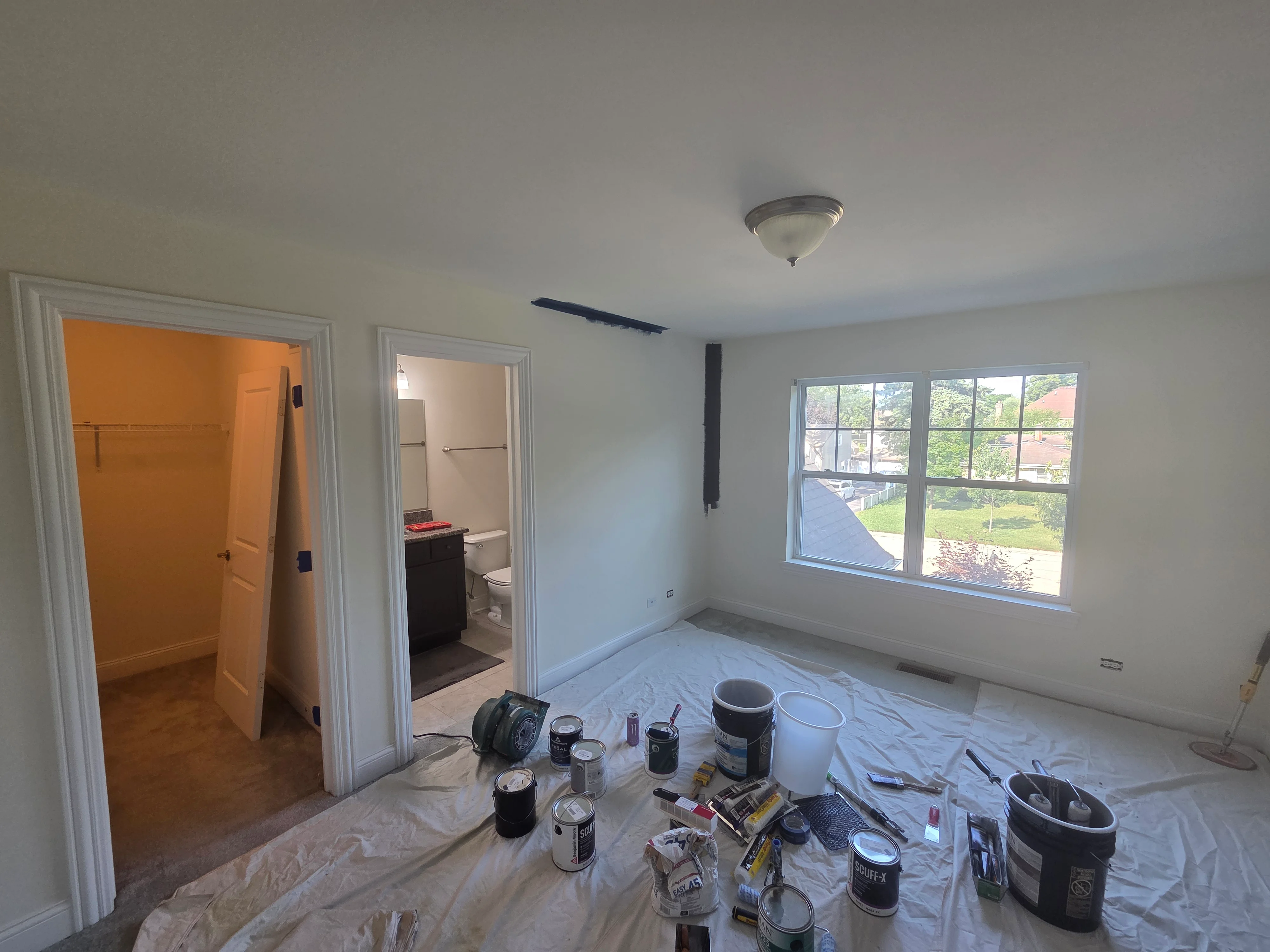 Bedroom interior with freshly painted white walls and ceiling, paint cans and supplies on drop cloth