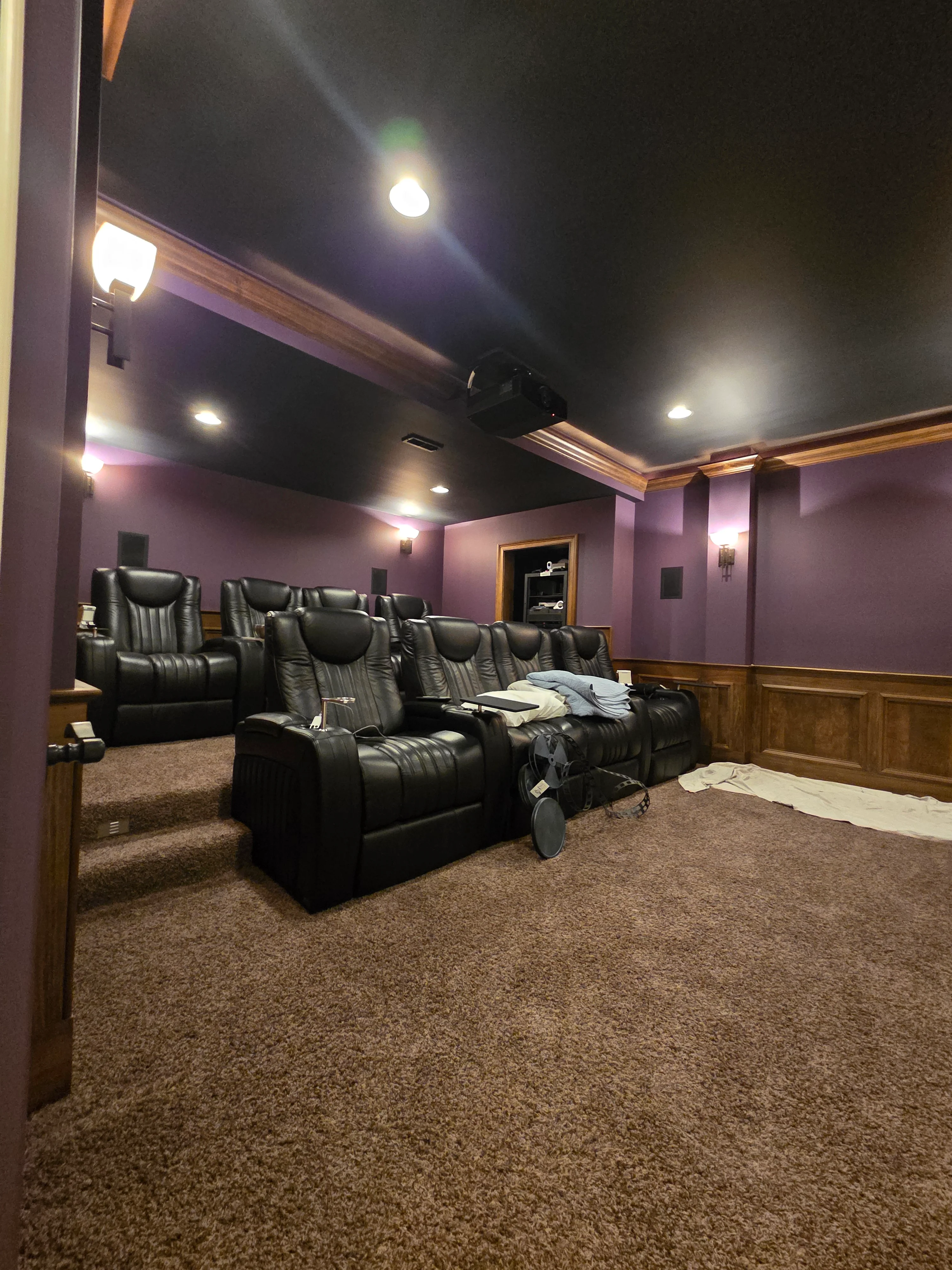 Purple painted walls with black ceiling, recessed lighting, and wood wainscoting in home theater room