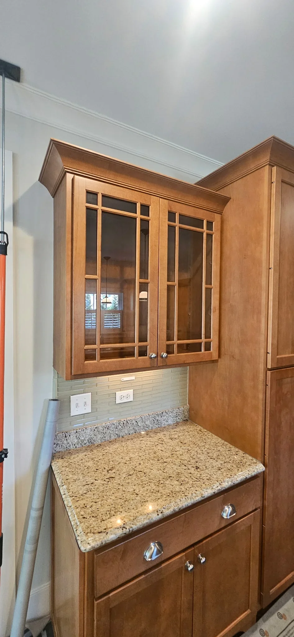 Stained wood kitchen cabinets with glass doors, granite countertop, and green subway tile backsplash