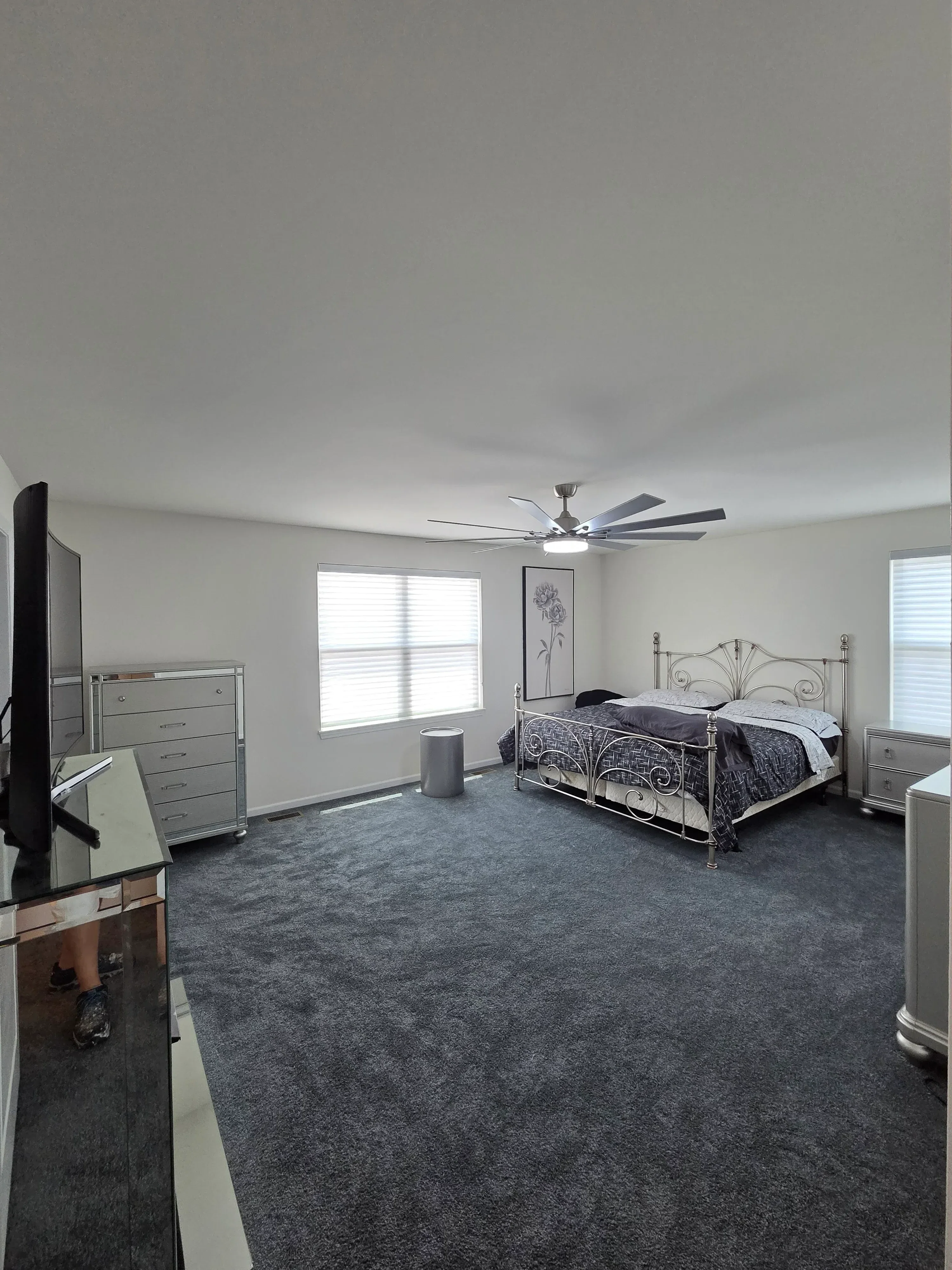 Bedroom with white painted walls, gray carpet, and iron bed frame with decorative headboard