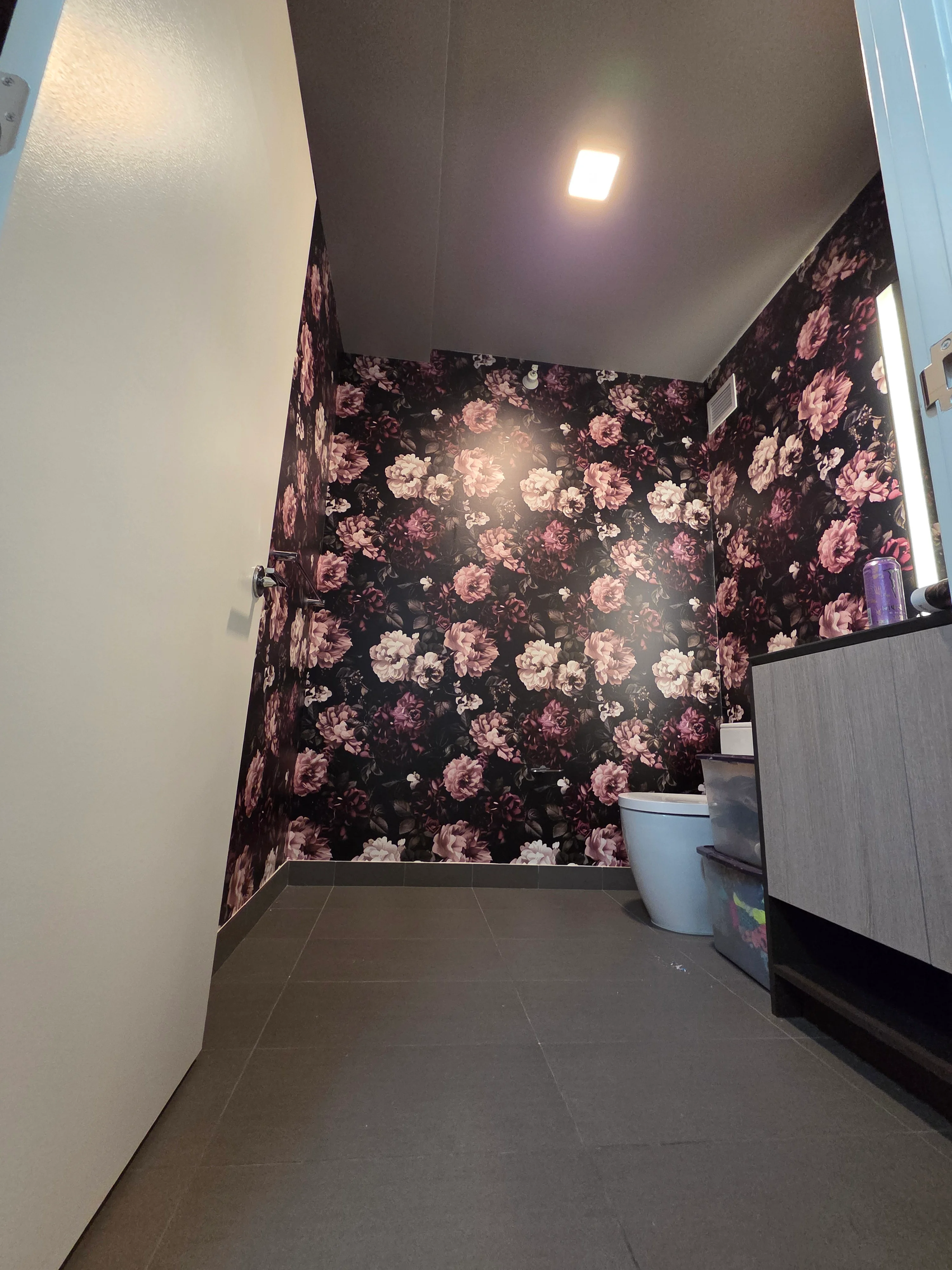 Dark floral wallpaper with pink roses installed on bathroom walls, white ceiling with recessed lighting