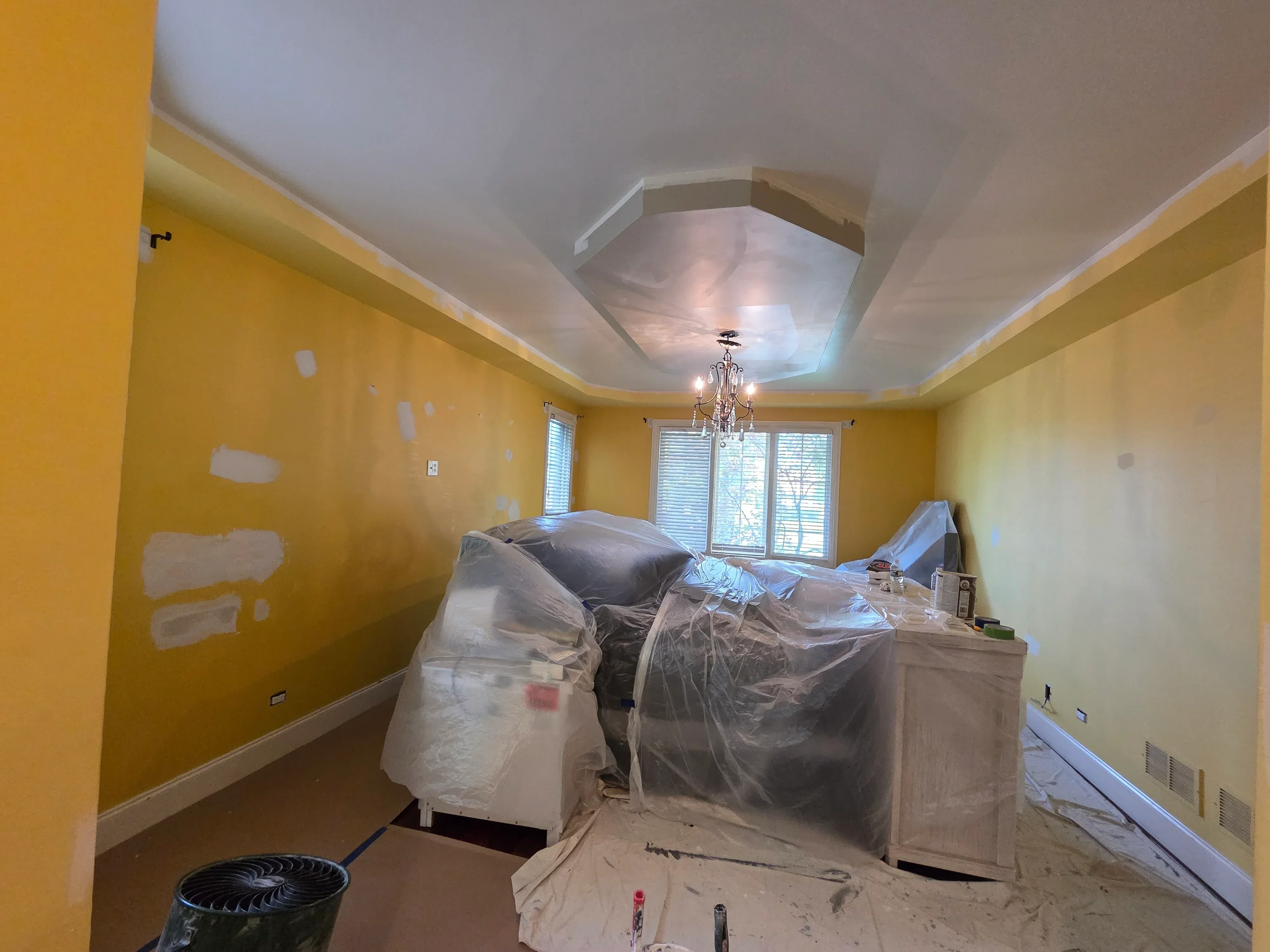 Interior room with yellow painted walls, white drywall ceiling, and protective plastic sheeting during renovation