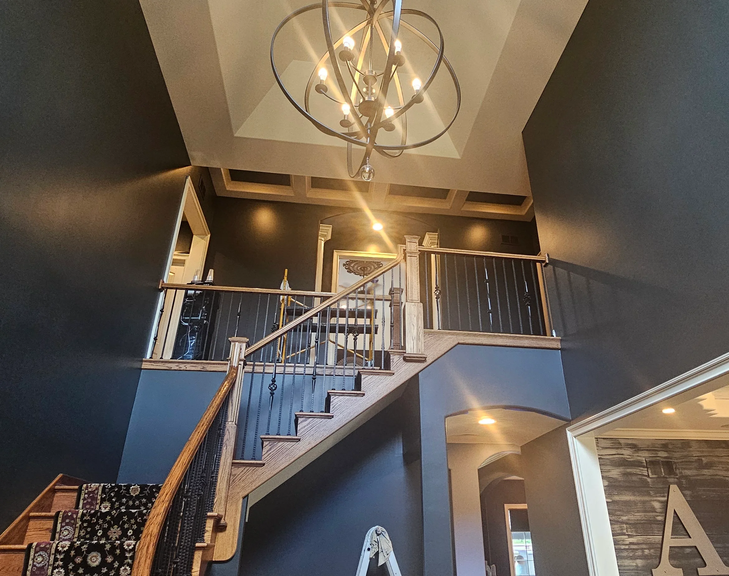 Two-story foyer with dark painted accent walls, white trim, wood staircase, and ceiling-mounted pendant light