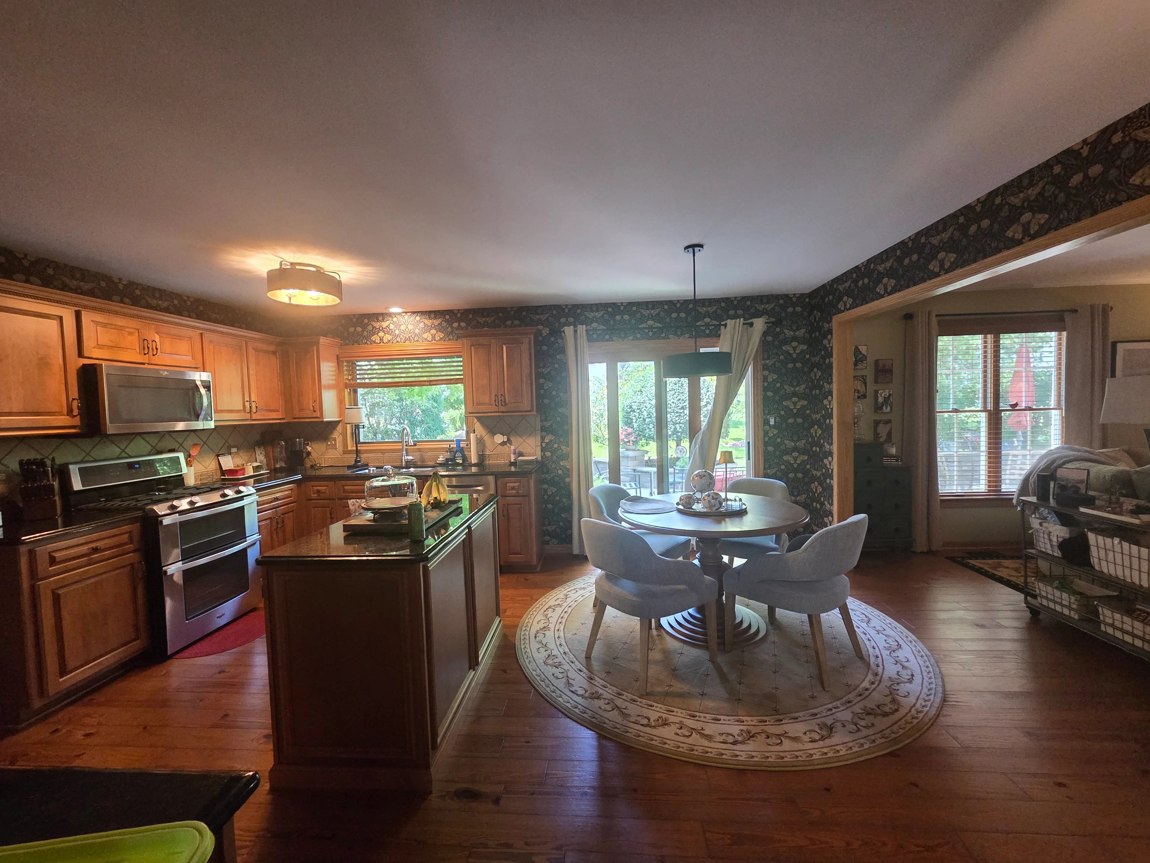 Kitchen with wood cabinetry, stainless steel appliances, and dining area with painted ceiling and teal floral wallpaper accent walls