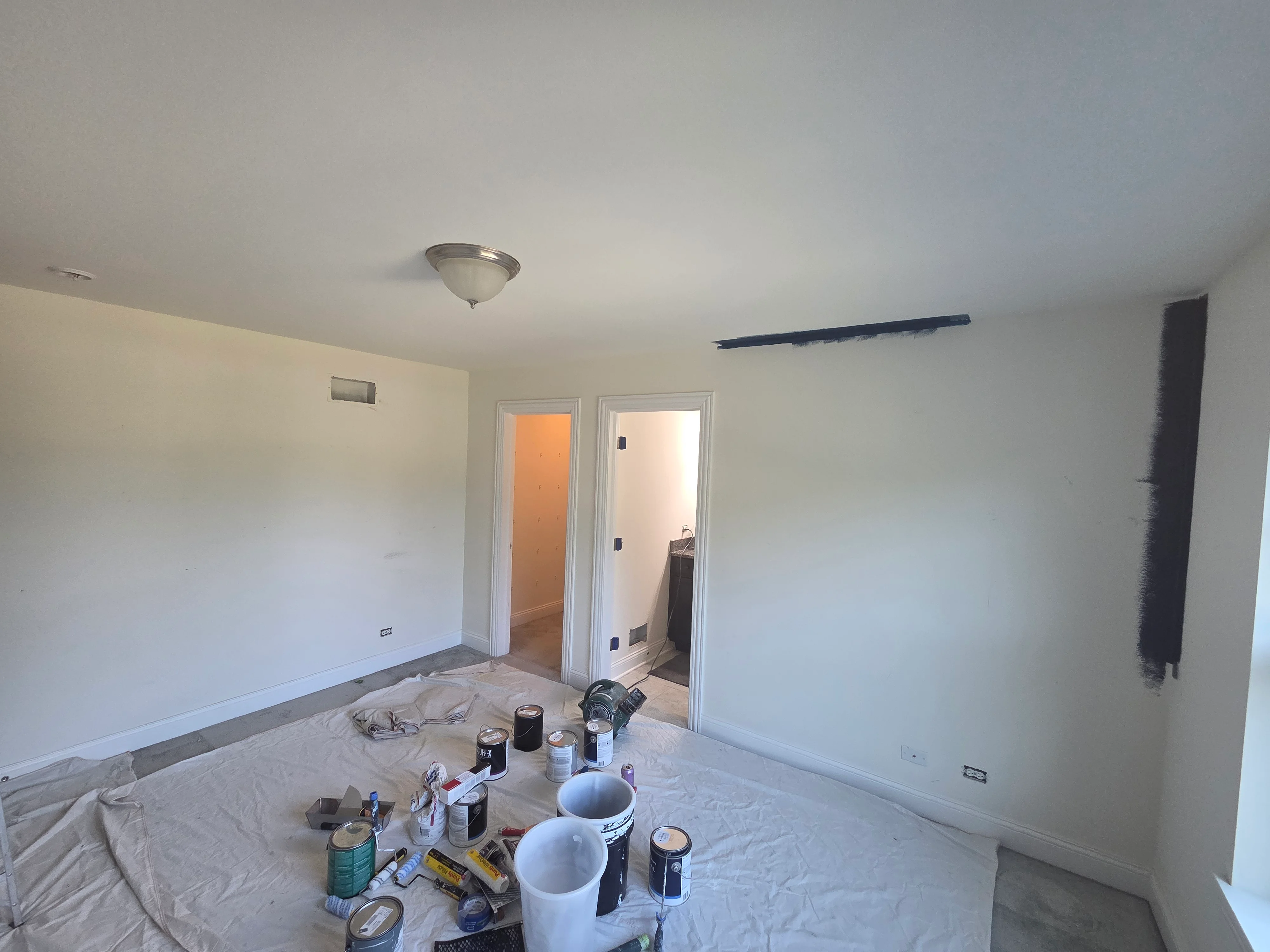Interior room with freshly painted white drywall walls, white trim, ceiling fixture, and painting supplies on drop cloths