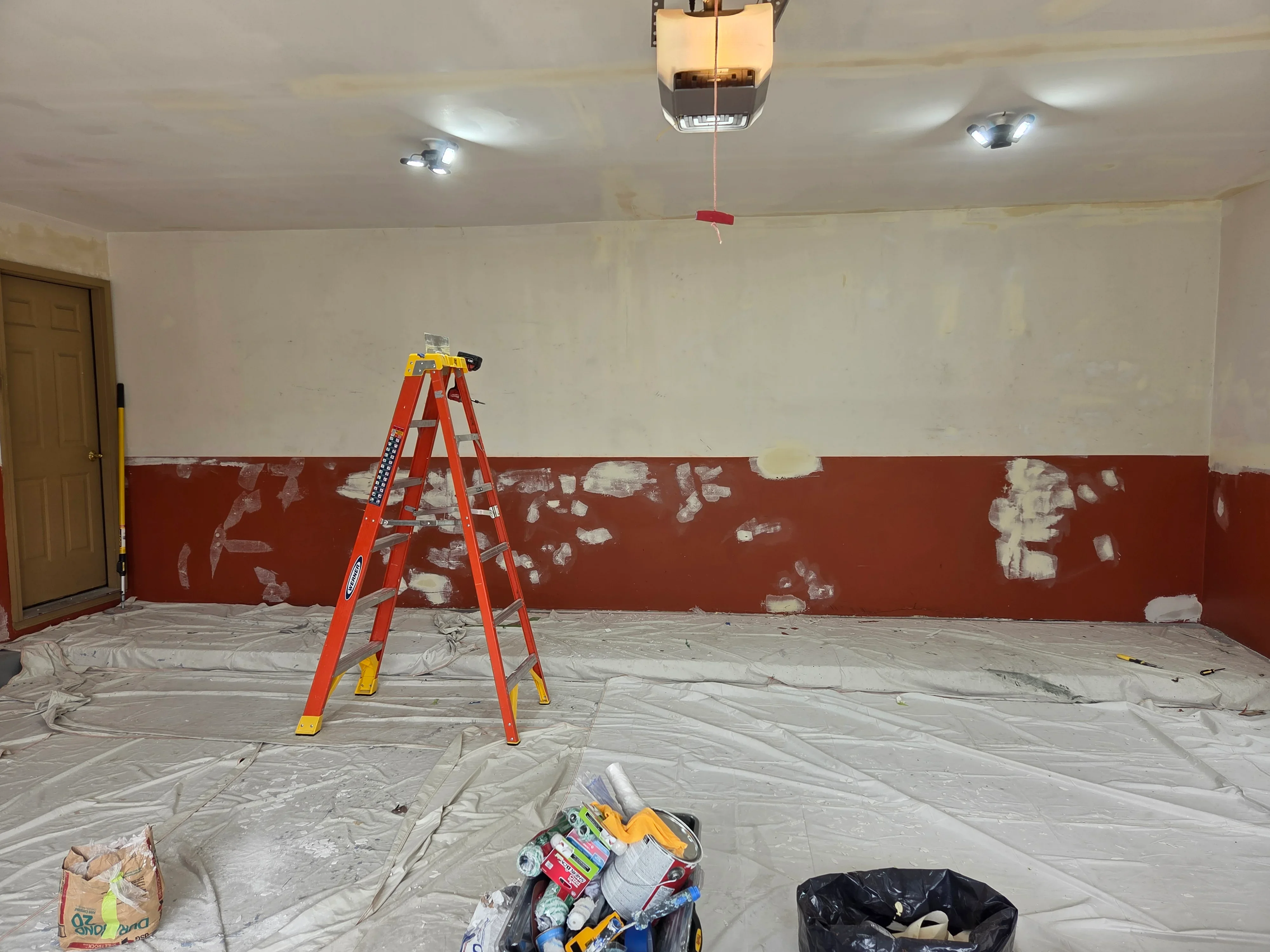 Interior room with red and cream two-tone walls, drywall prep work, drop cloths, and painting equipment