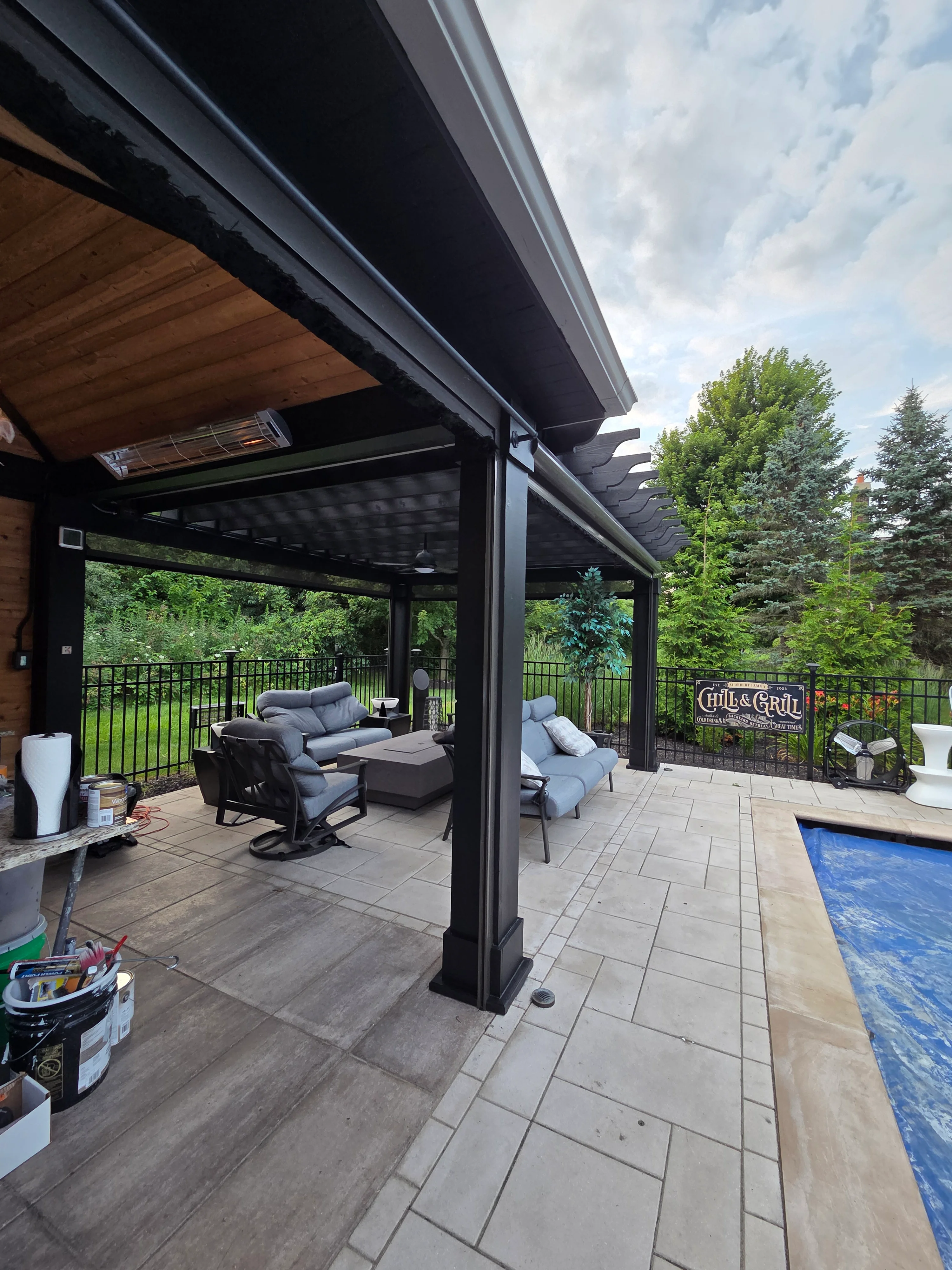 Black pergola with retractable shade, metal railings, and painted patio surfaces overlooking landscaped yard