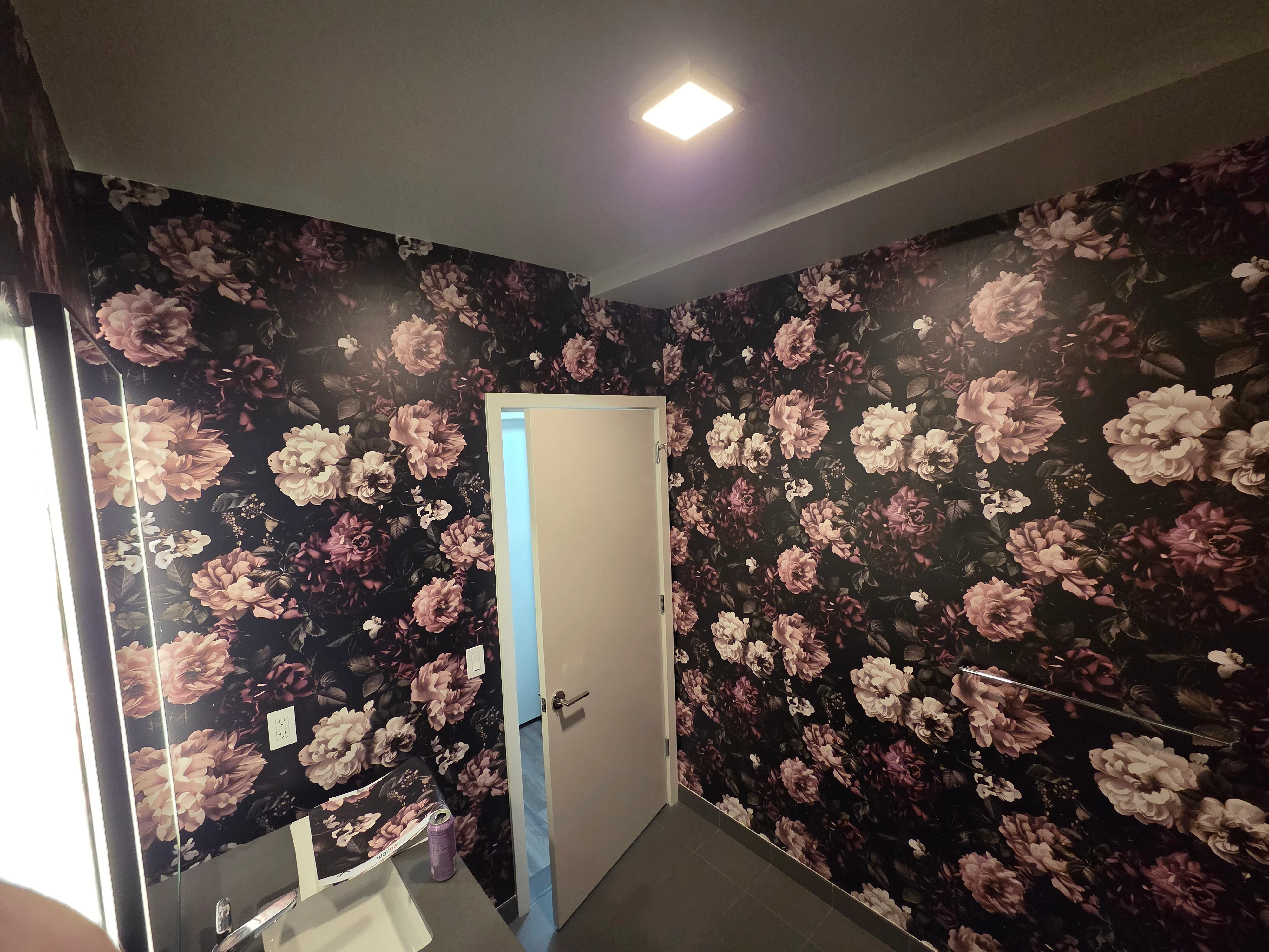 Dark floral wallpaper with pink and cream roses installed in bathroom with white trim and recessed lighting
