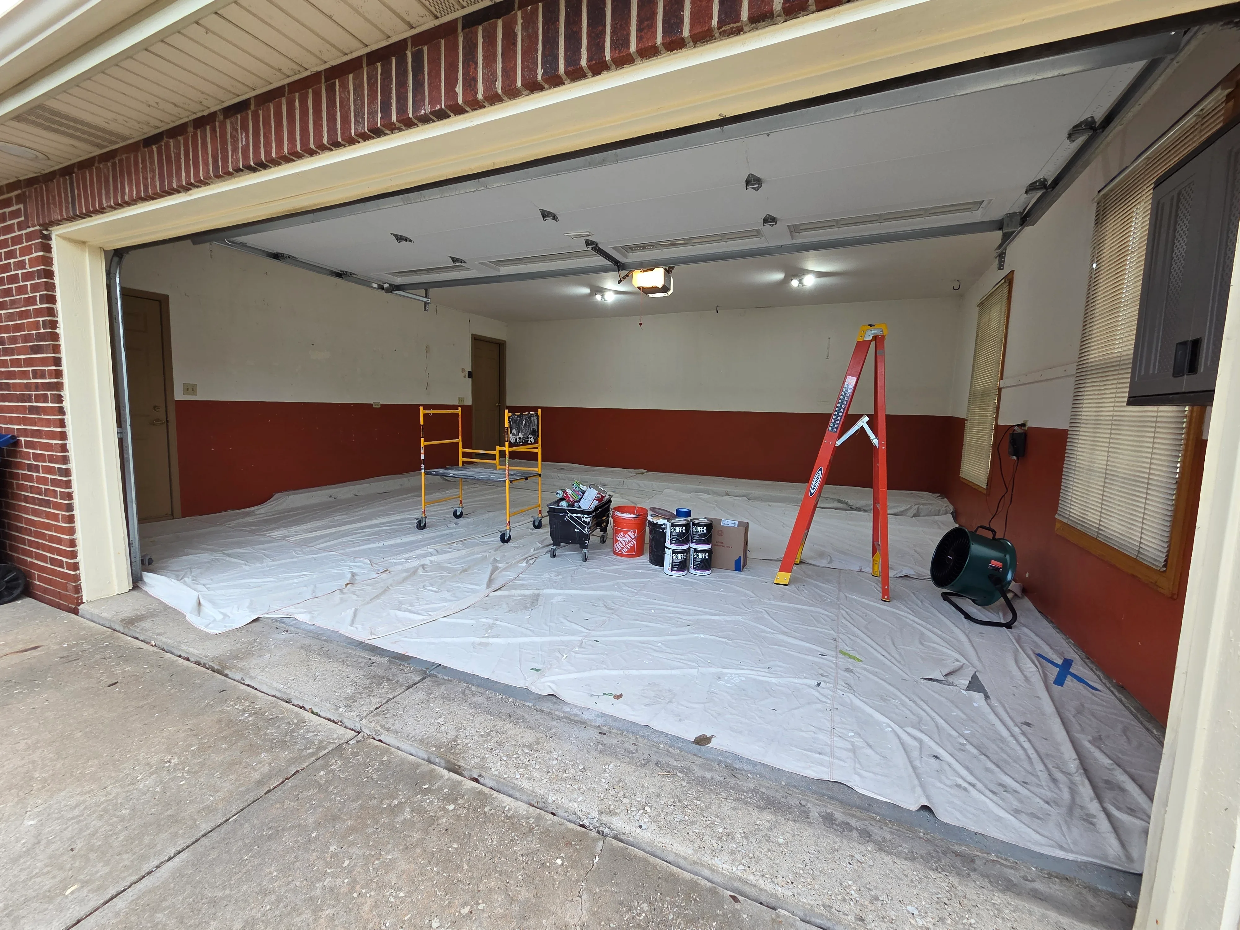 Garage interior with two-tone red and white painted walls, protective drop cloths, and LED ceiling lights