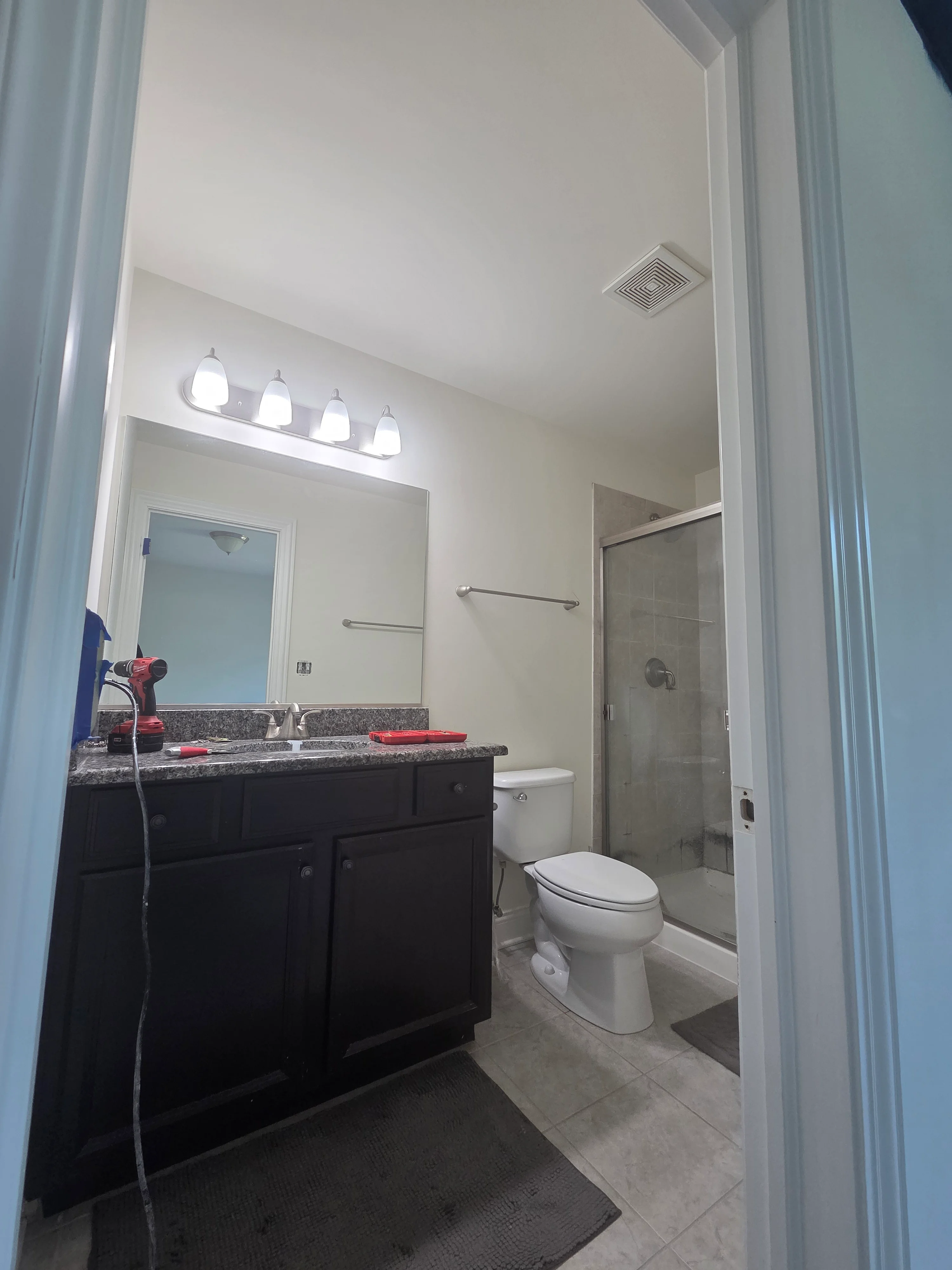 Freshly painted bathroom with white walls and ceiling, dark vanity cabinet, granite countertop, and glass shower enclosure
