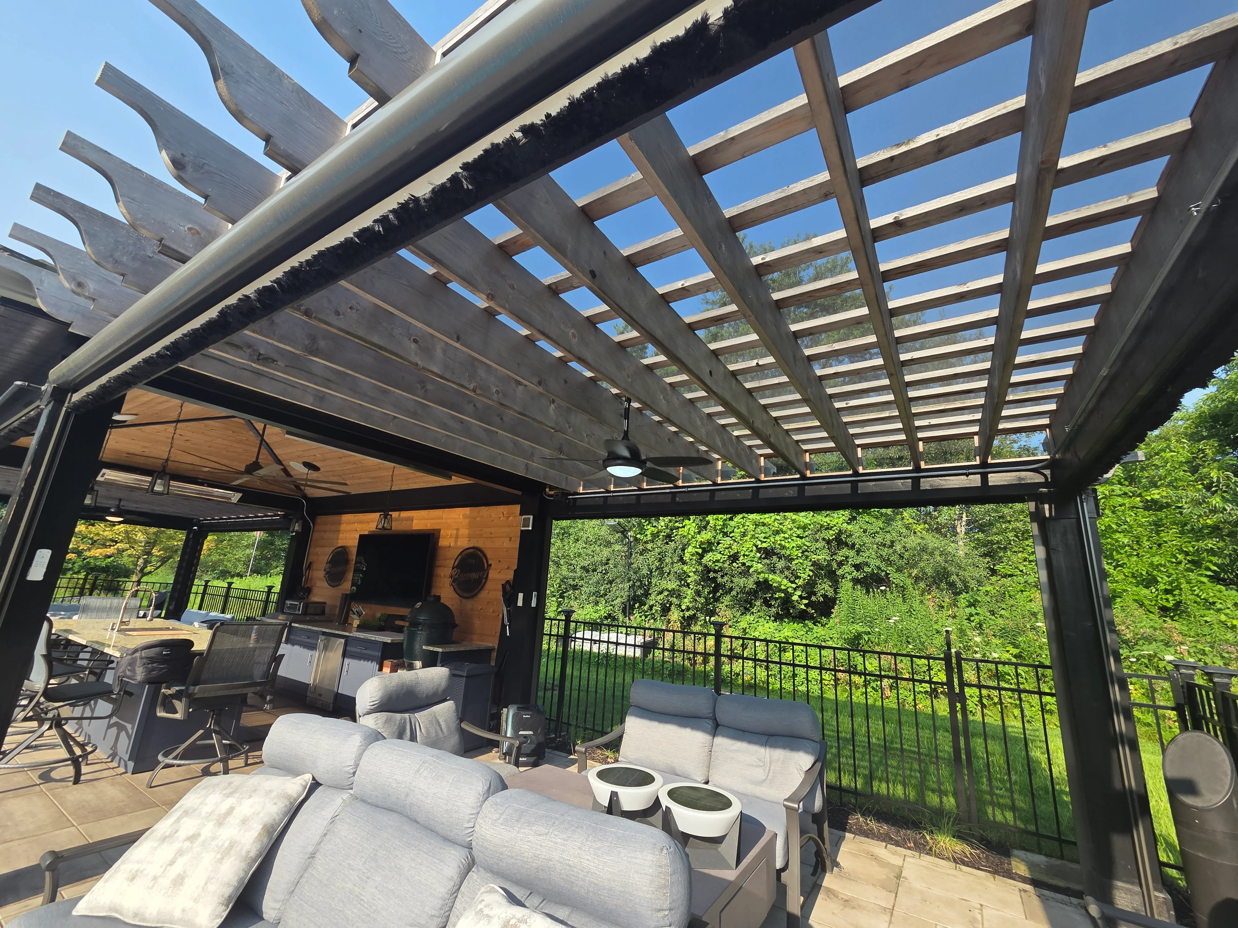 Gray steel pergola with wooden lattice, outdoor seating area, wood accent wall, and black metal railings