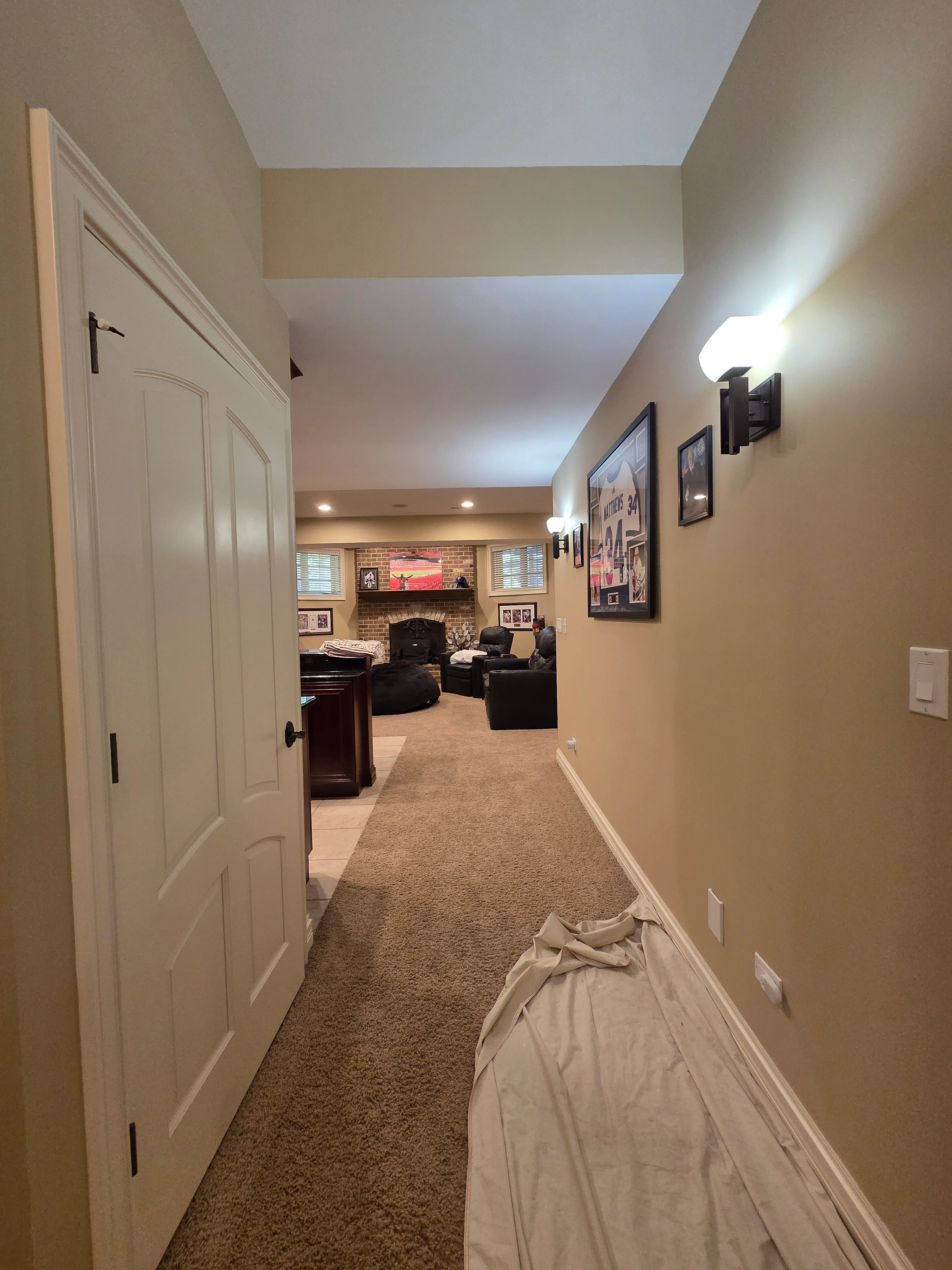 Painted basement hallway with cream walls, white trim doors, and recessed ceiling lights leading to recreation room