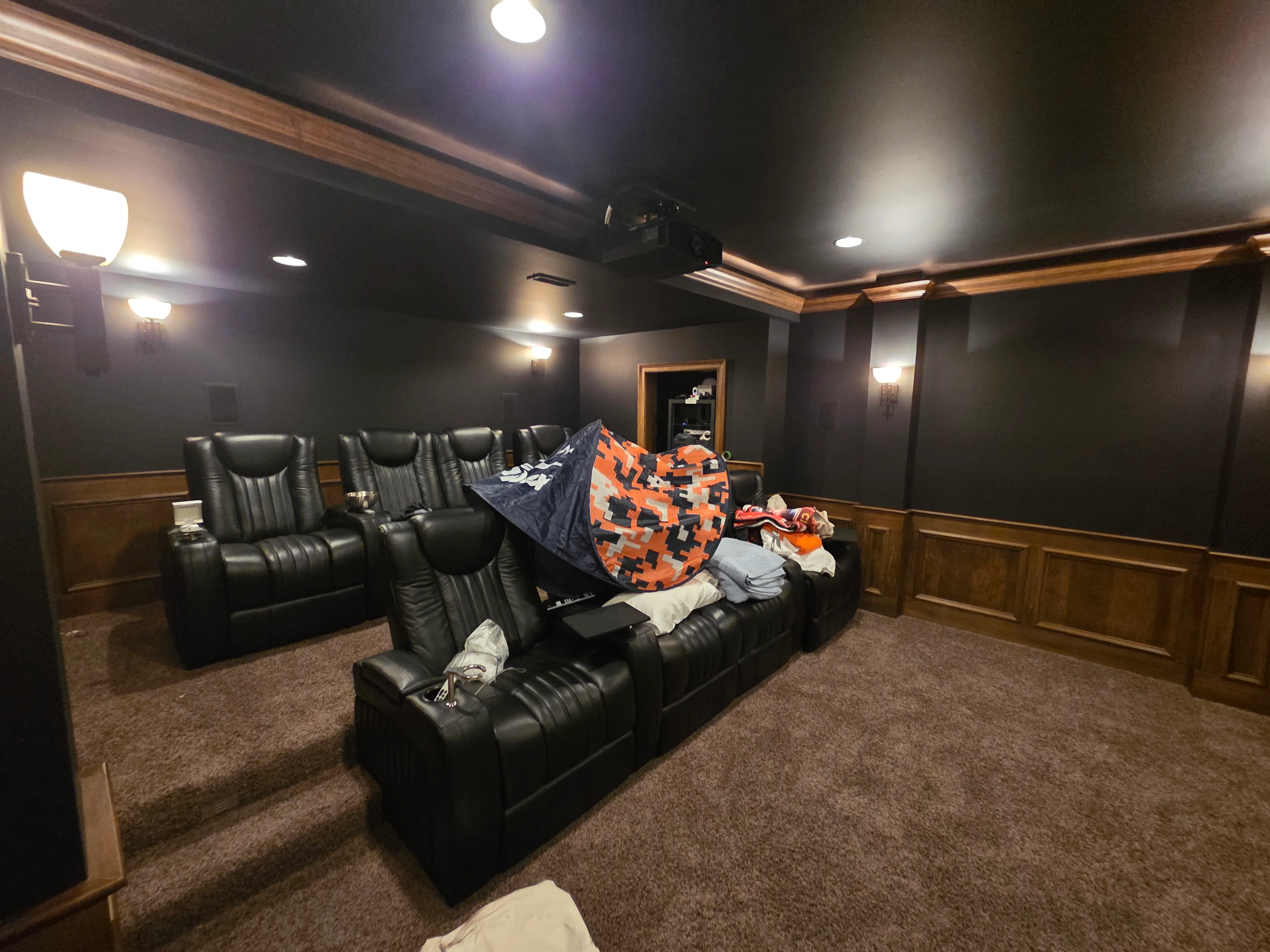 Dark charcoal painted walls with wood wainscoting, wood ceiling beams, recessed lighting, and wall sconces in home theater room
