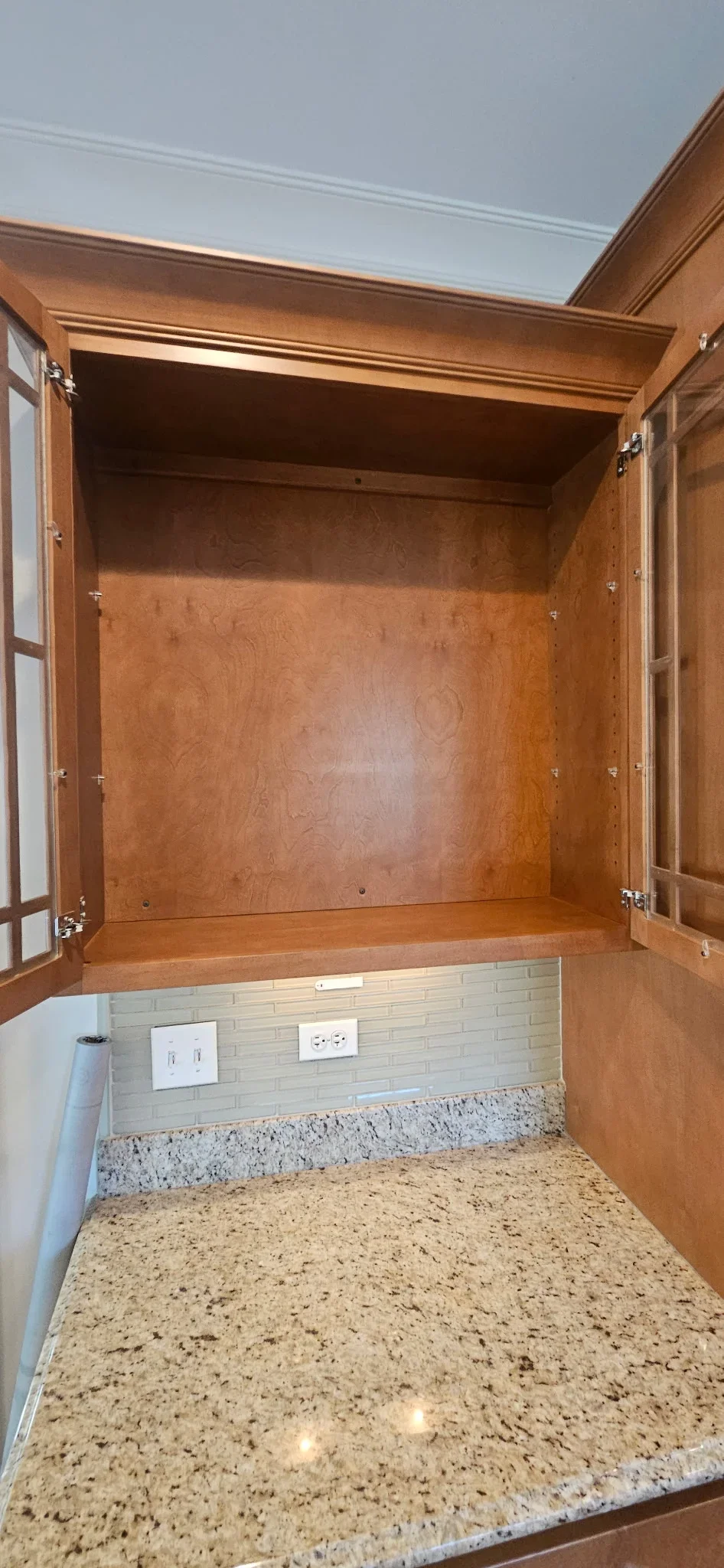 Open cherry wood kitchen cabinet with white subway tile backsplash and speckled granite countertop