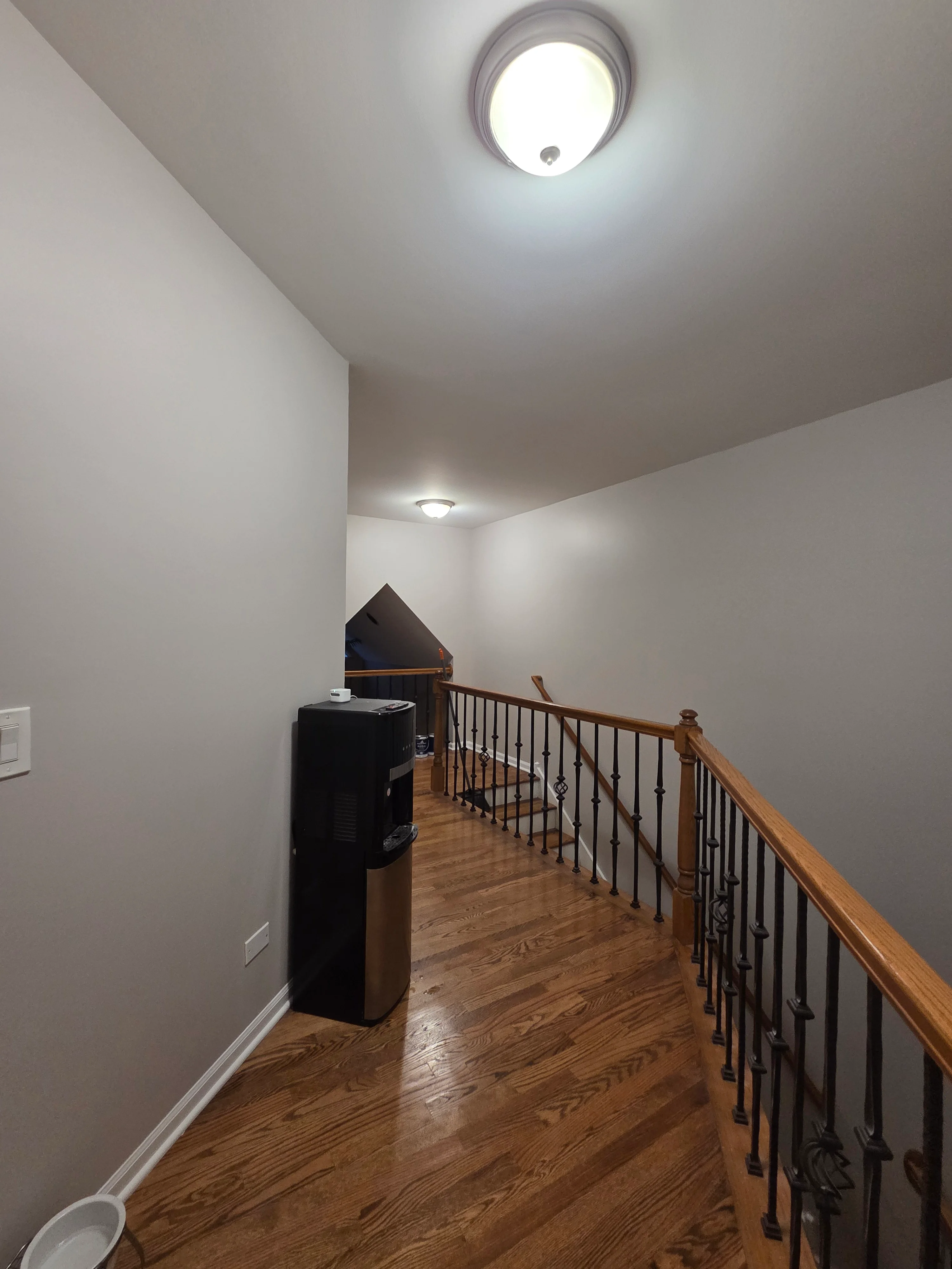 Painted upper landing hallway with gray walls, white ceiling, wood flooring, and stair railing