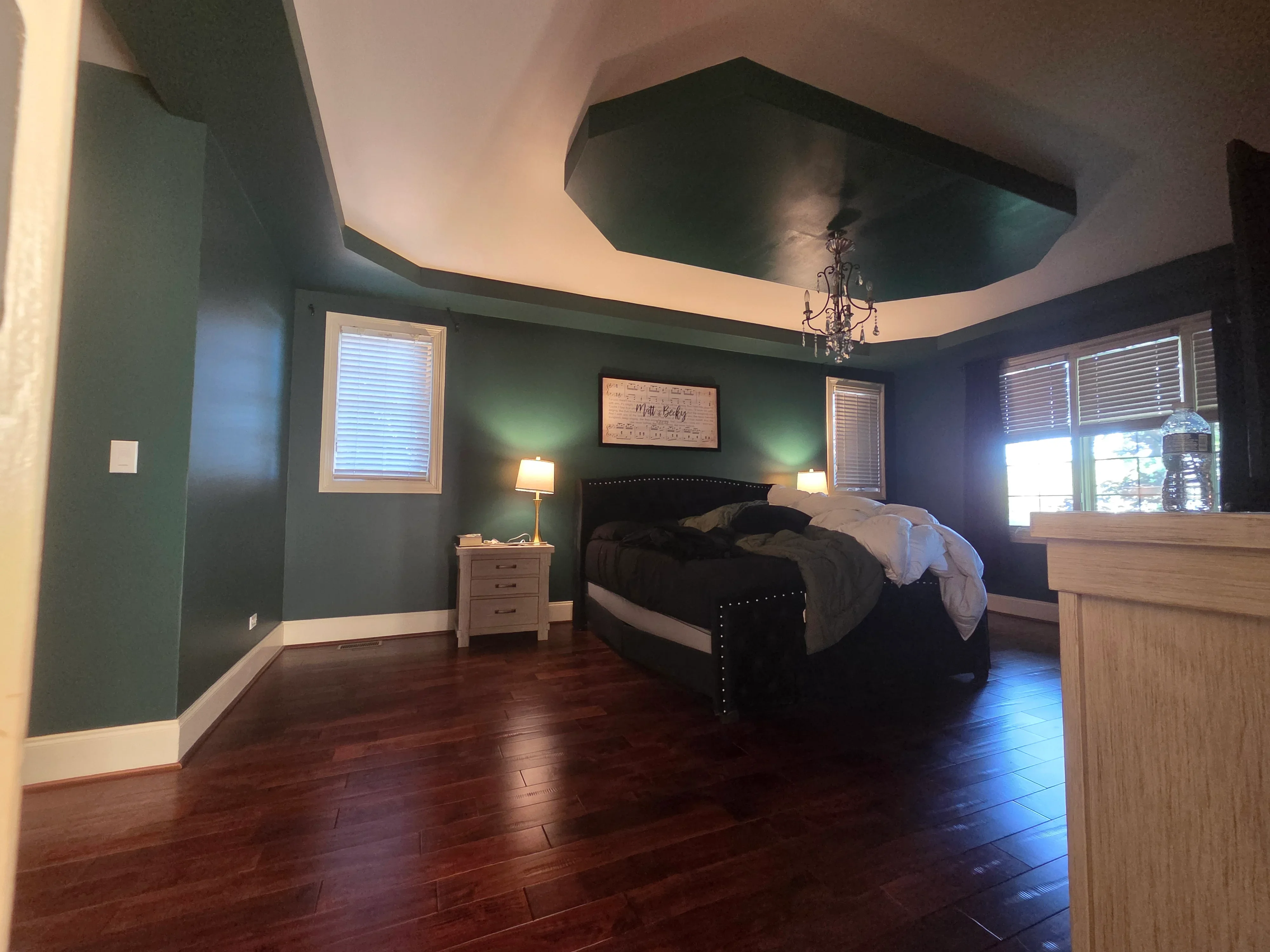 Master bedroom with forest green walls, white trim, curved ceiling with chandelier, hardwood floors