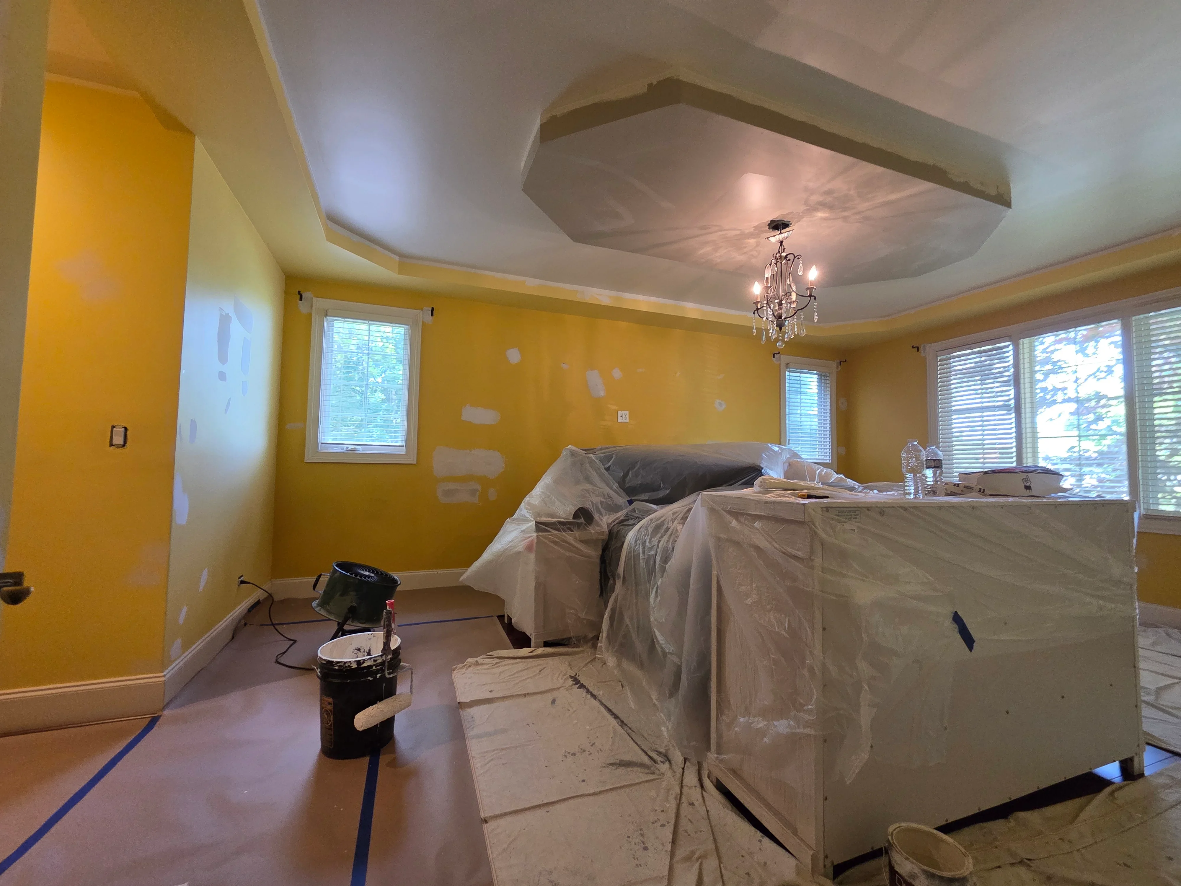 Master bedroom with yellow walls, white trim, and white tray ceiling during painting project