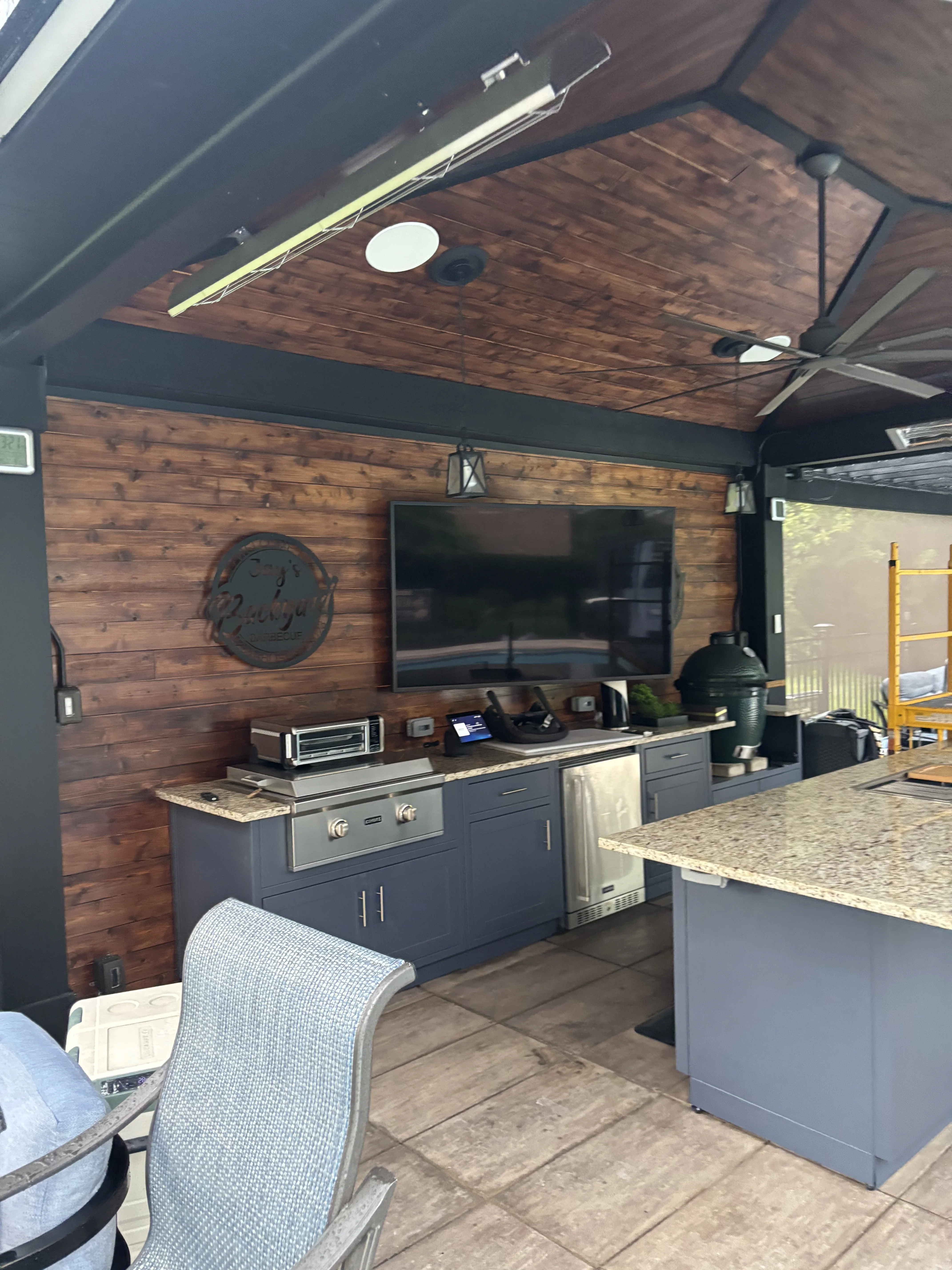 Dark gray cabinetry, reclaimed wood walls, wood ceiling with LED lighting in outdoor kitchen