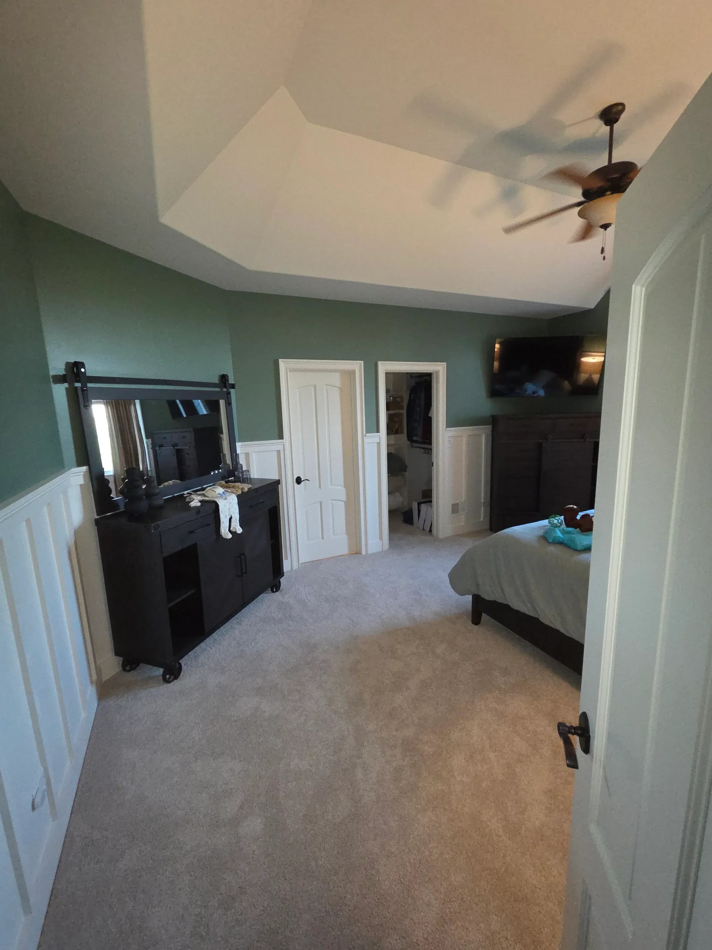Bedroom with sage green accent wall, white trim, and neutral side walls with painted ceiling