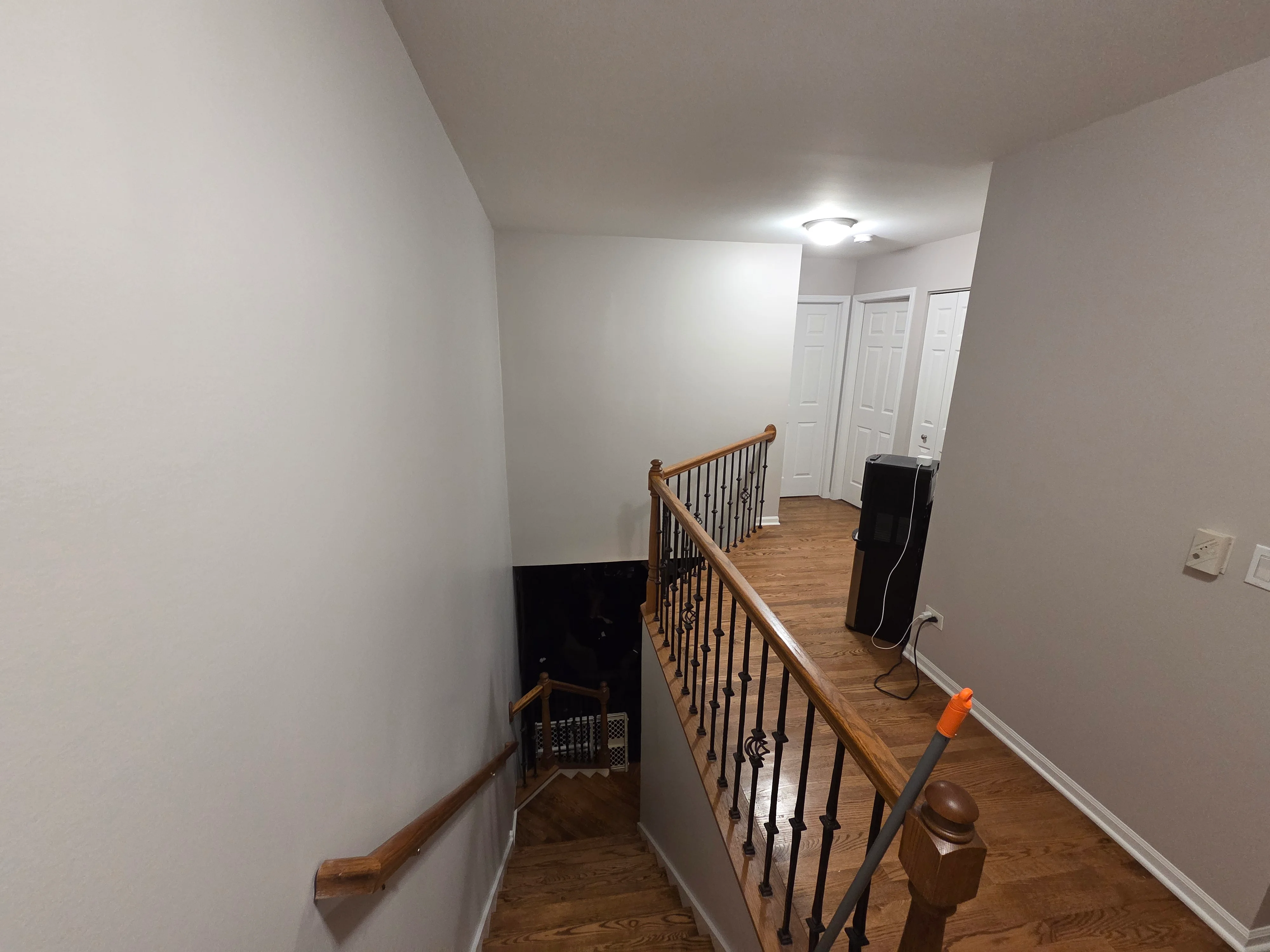 Freshly painted white stairwell with wood railing, hardwood floors, and white trim