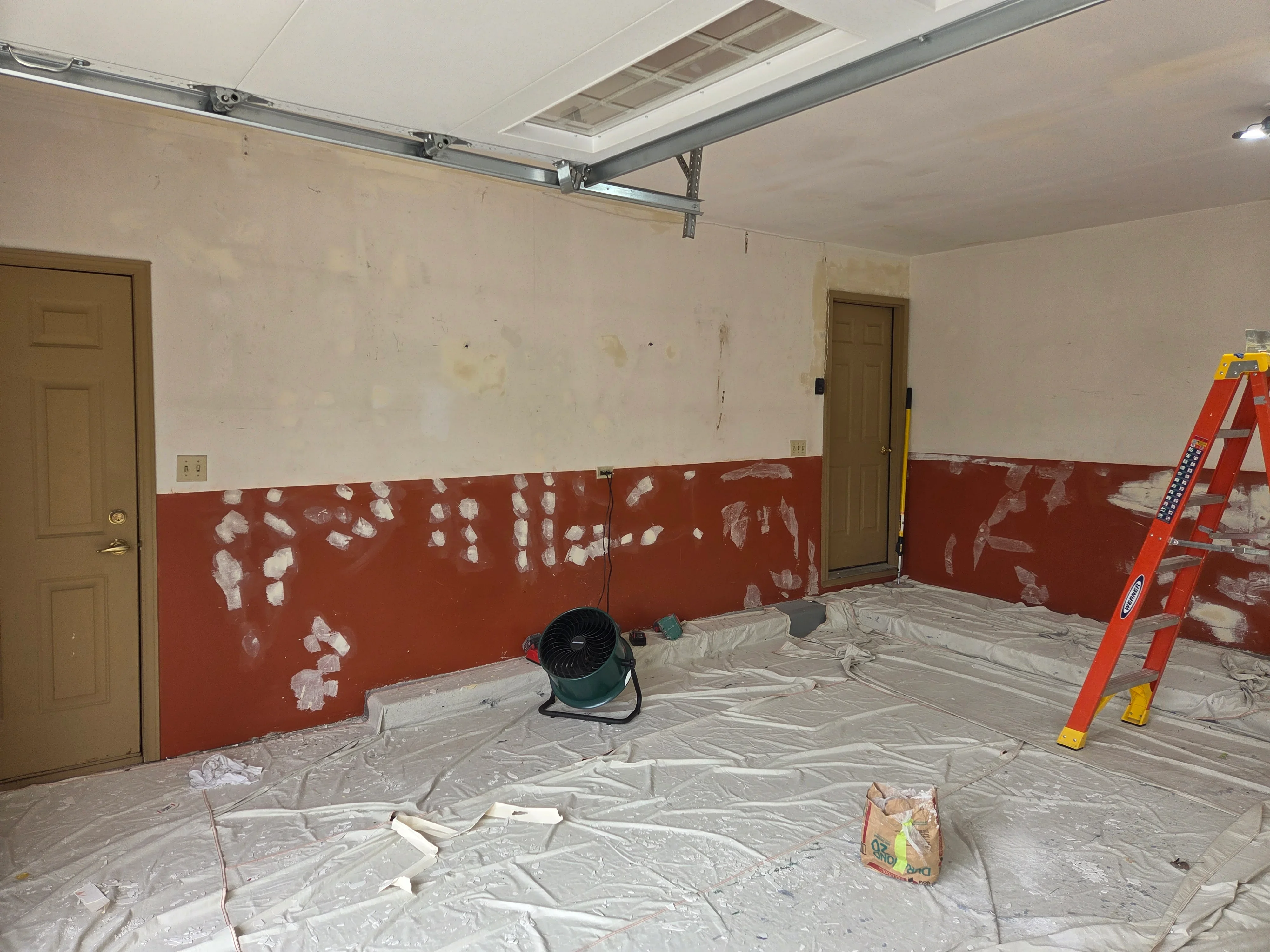 Garage drywall repair with red paint and compound patches on lower walls, primed upper section