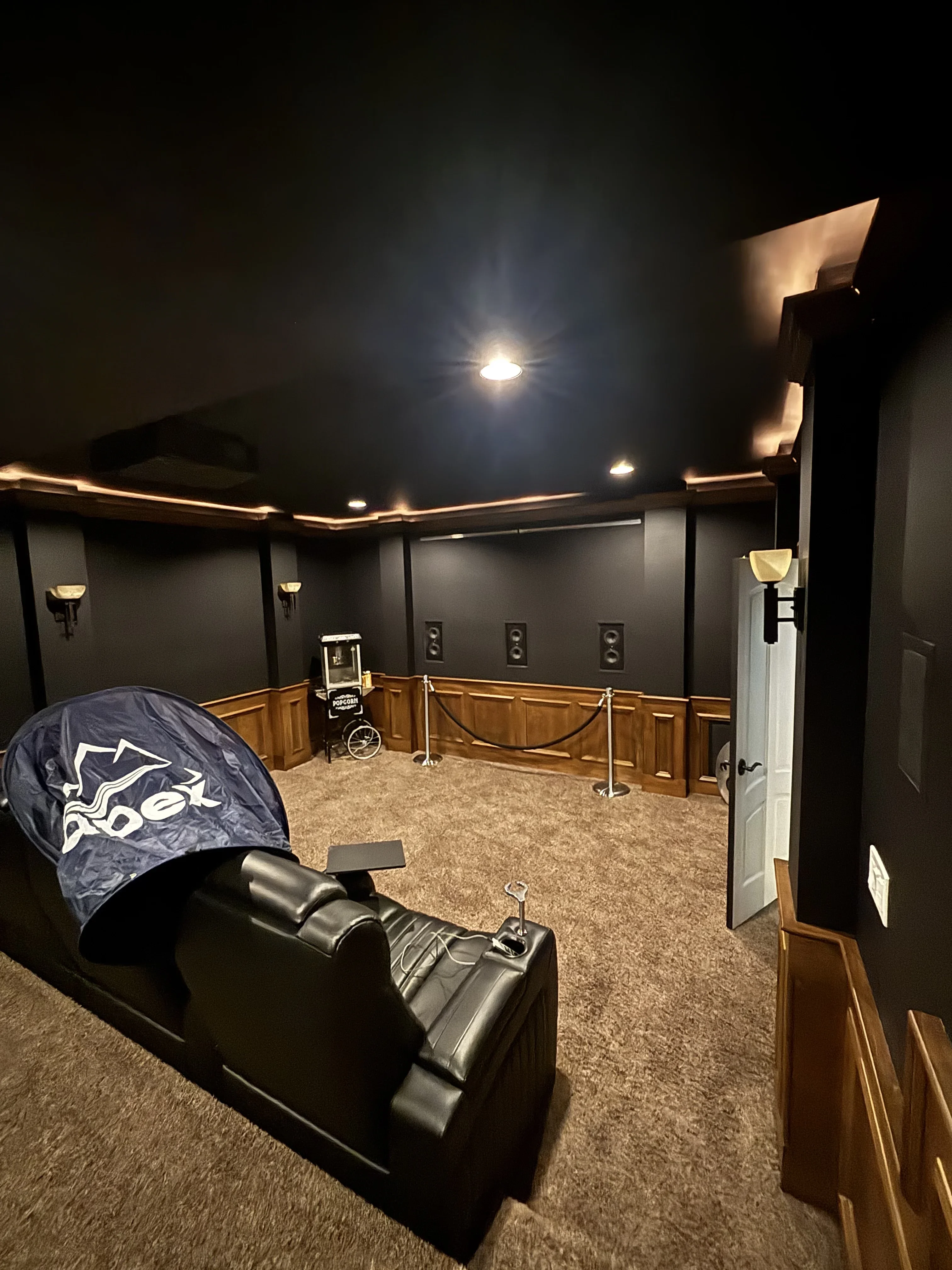 Dark painted home theater room with wood wainscoting, recessed and cove lighting, acoustic panels, and carpet flooring