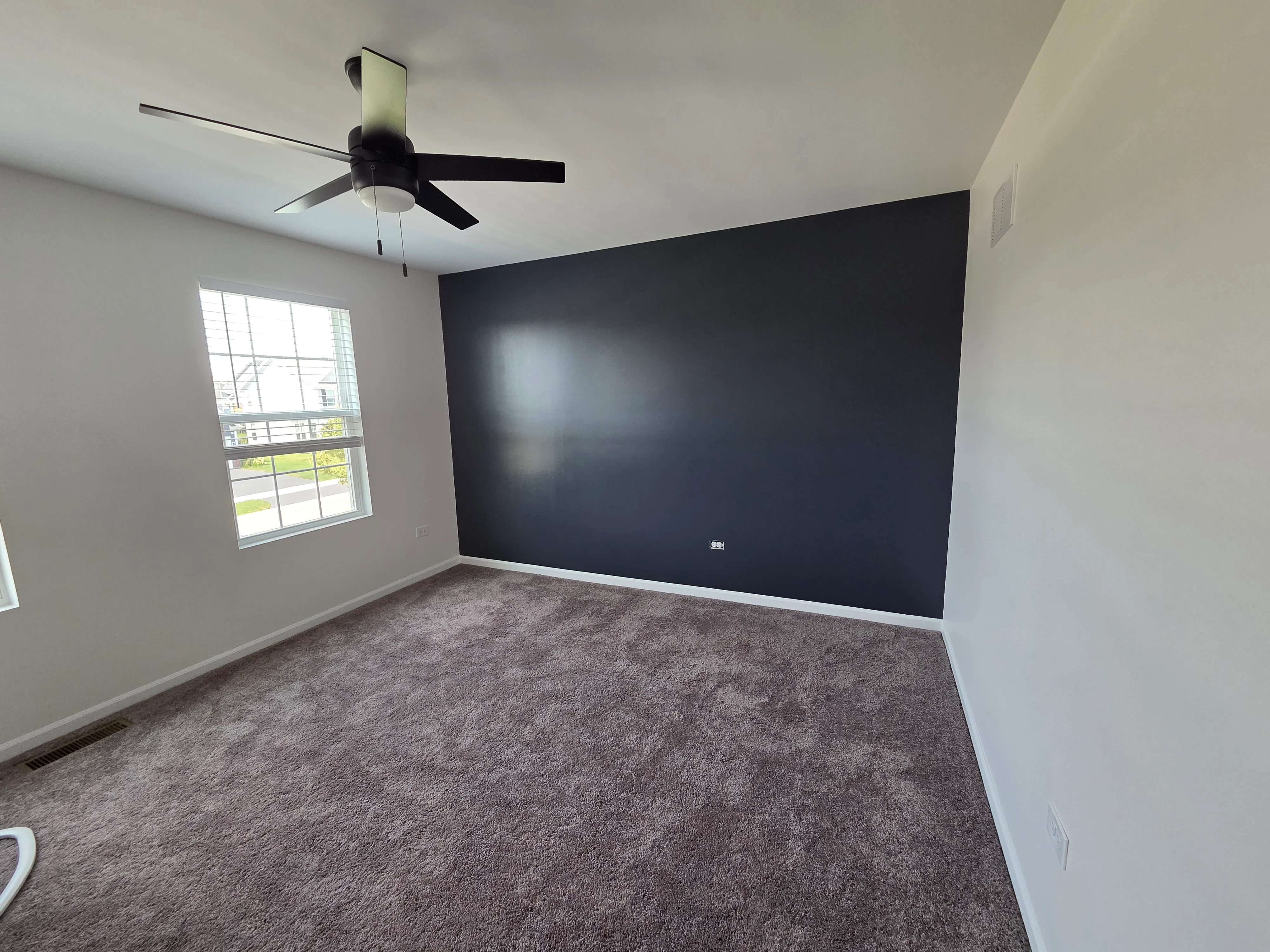 Charcoal accent wall with neutral walls, carpet flooring, and ceiling fan in bedroom