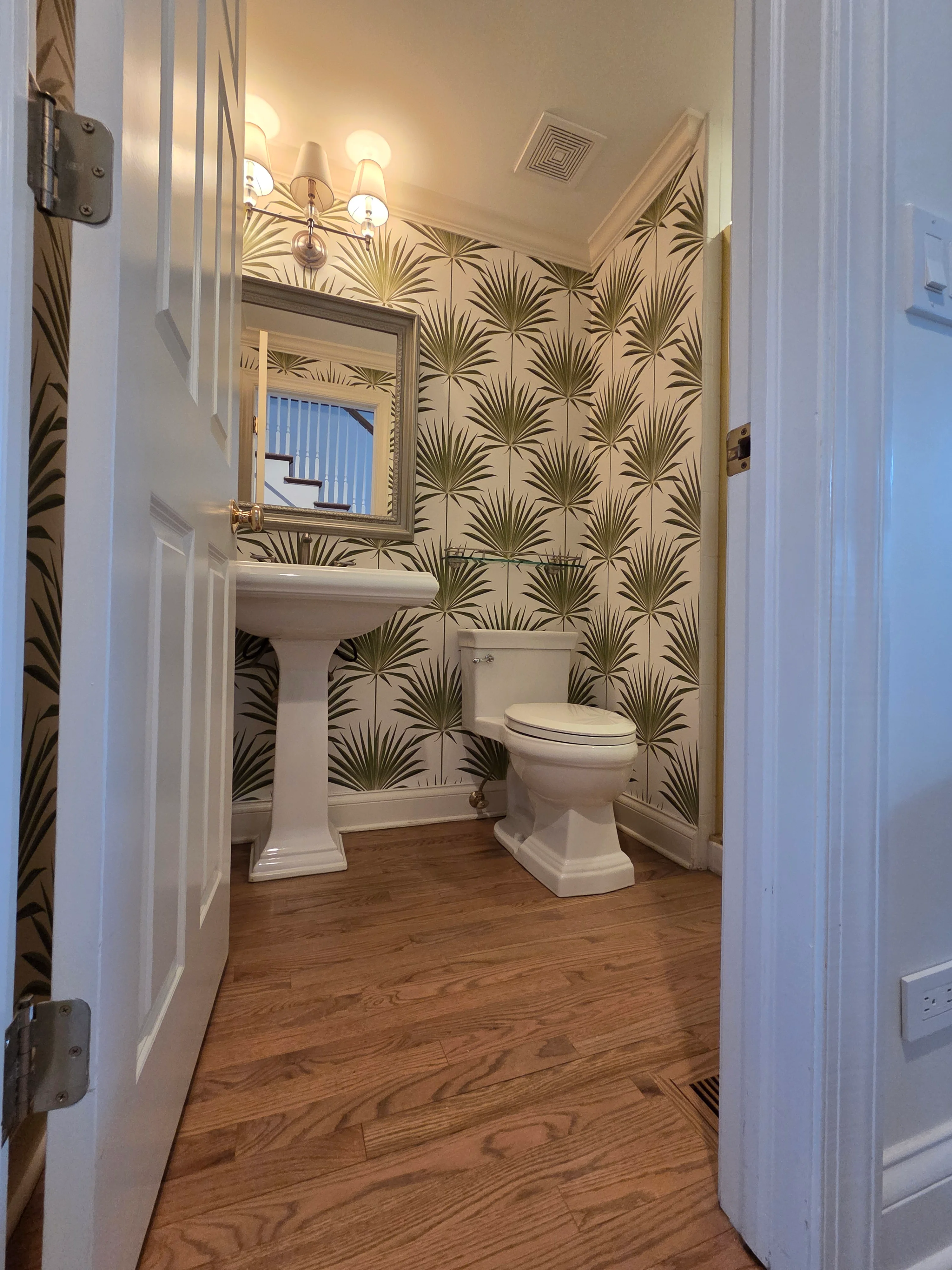 Powder room with cream and olive botanical wallpaper, pedestal sink, toilet, and framed mirror