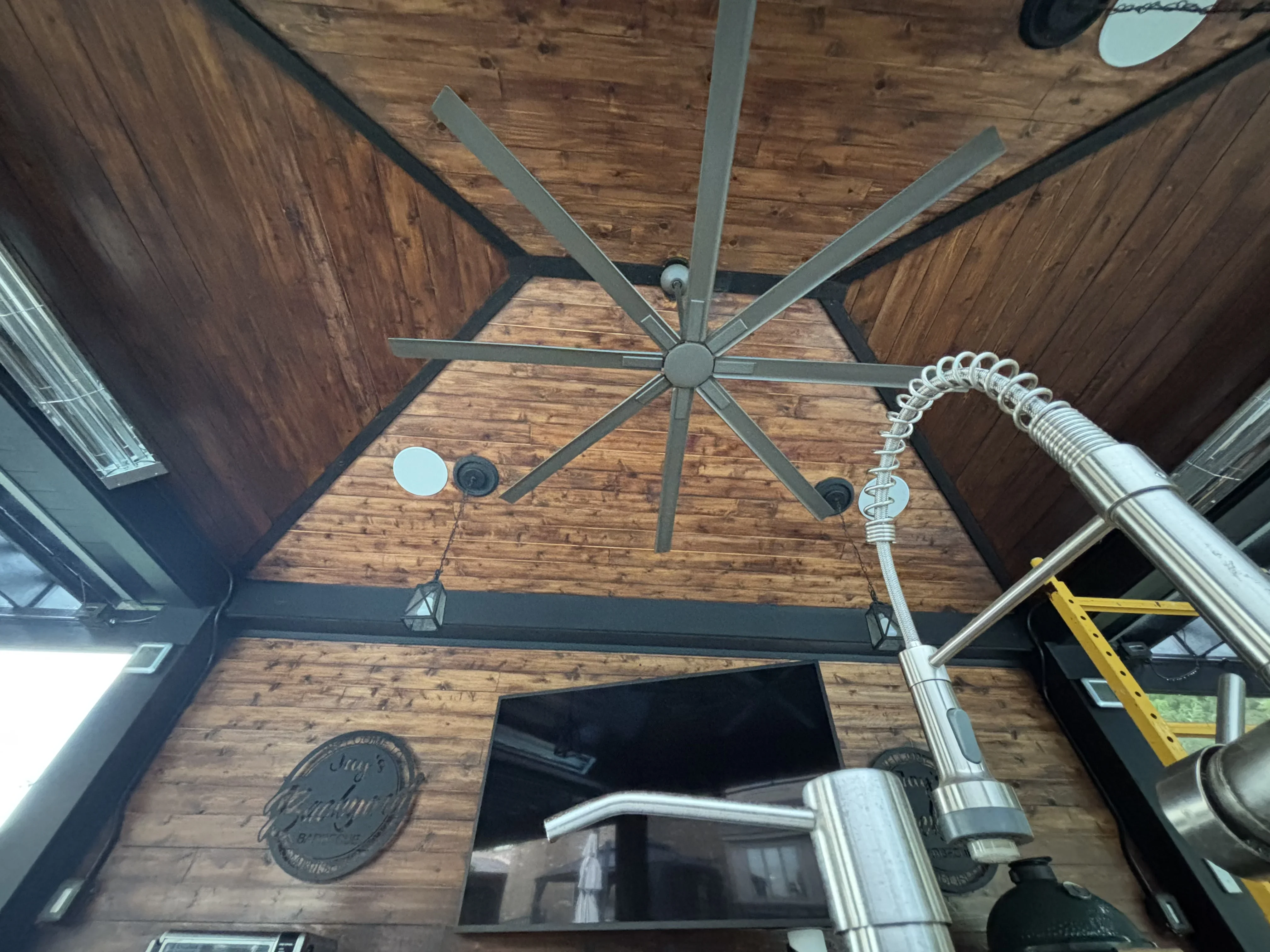 Stained wood vaulted ceiling with dark trim beams and brushed metal ceiling fan installation