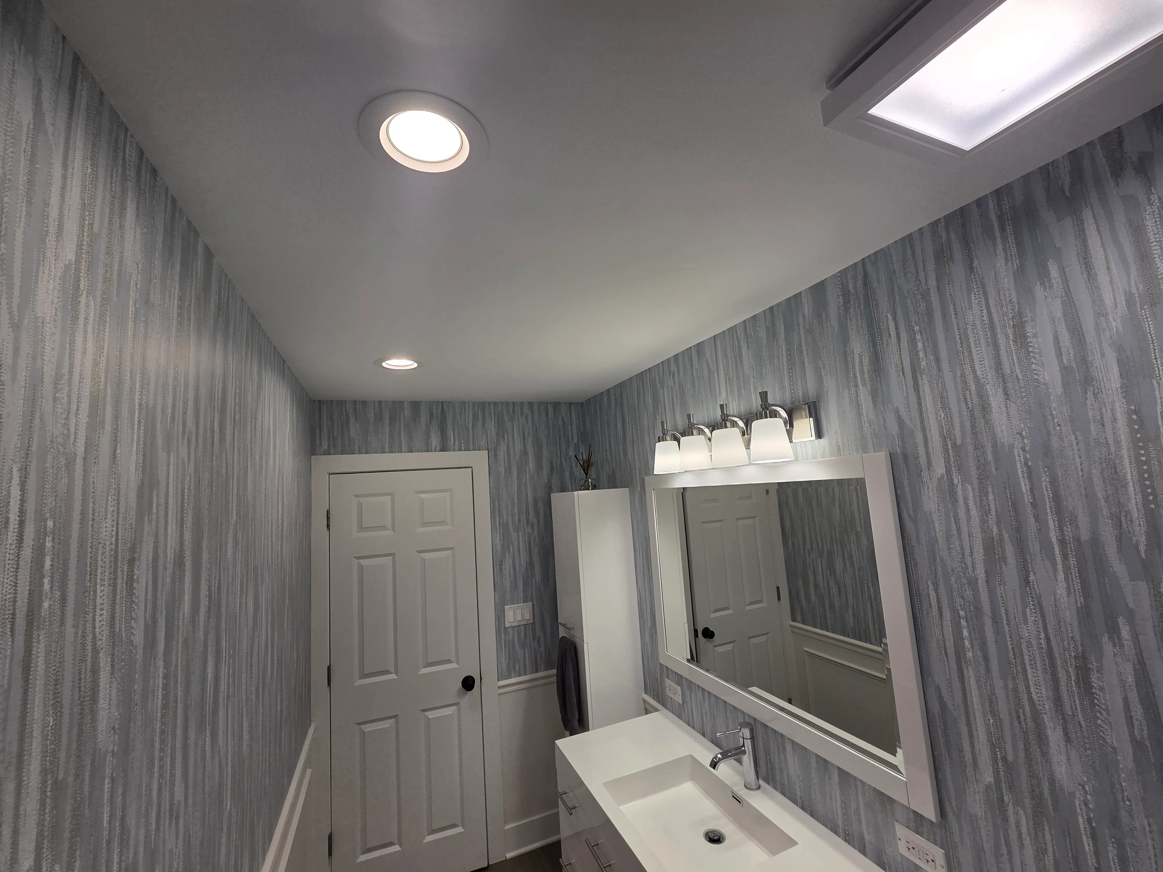 Gray striped wallpaper bathroom with white trim, recessed lighting, and vanity mirror