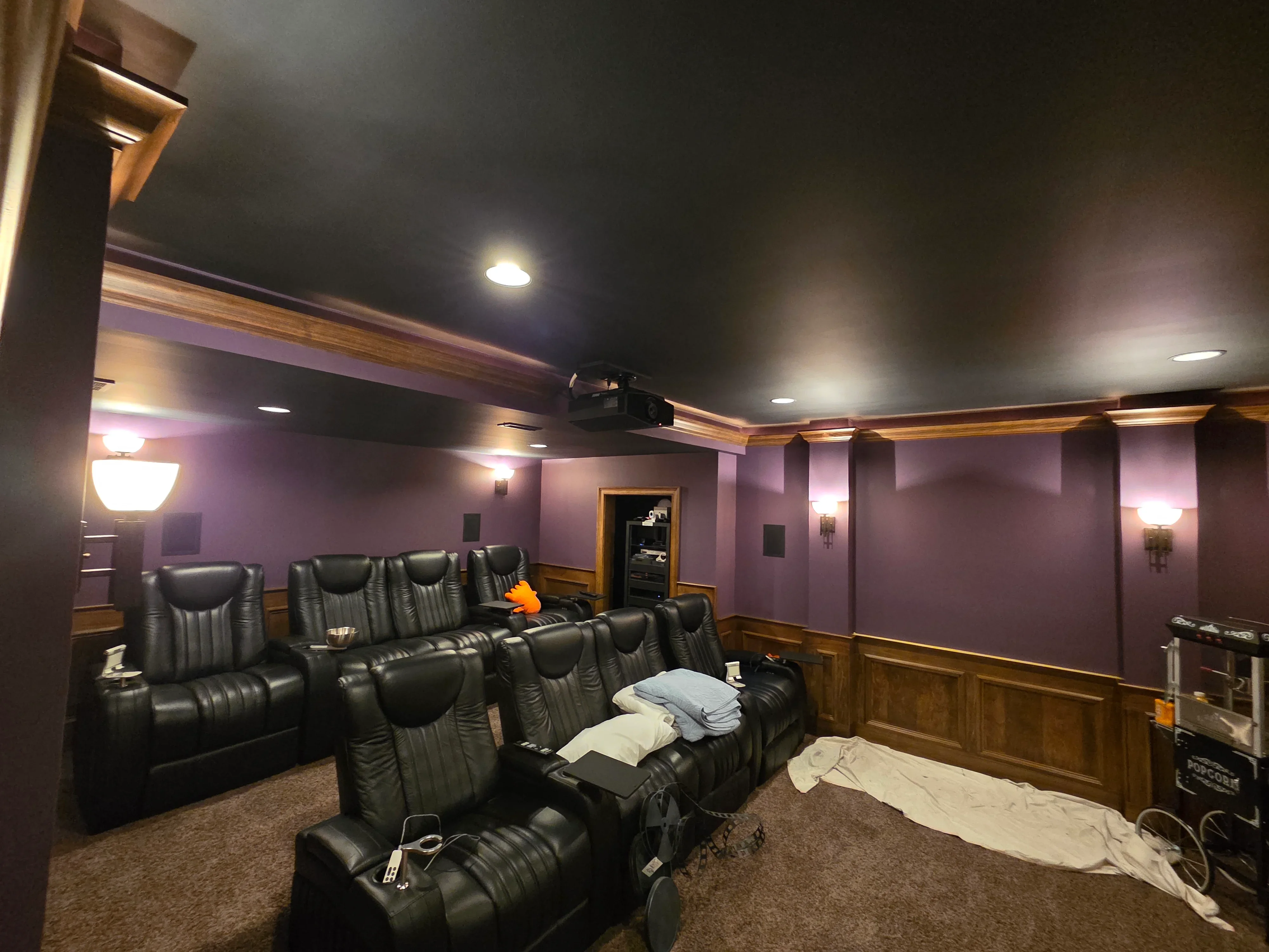 Purple painted home theater room with black leather seating, wood wainscoting, and recessed lighting