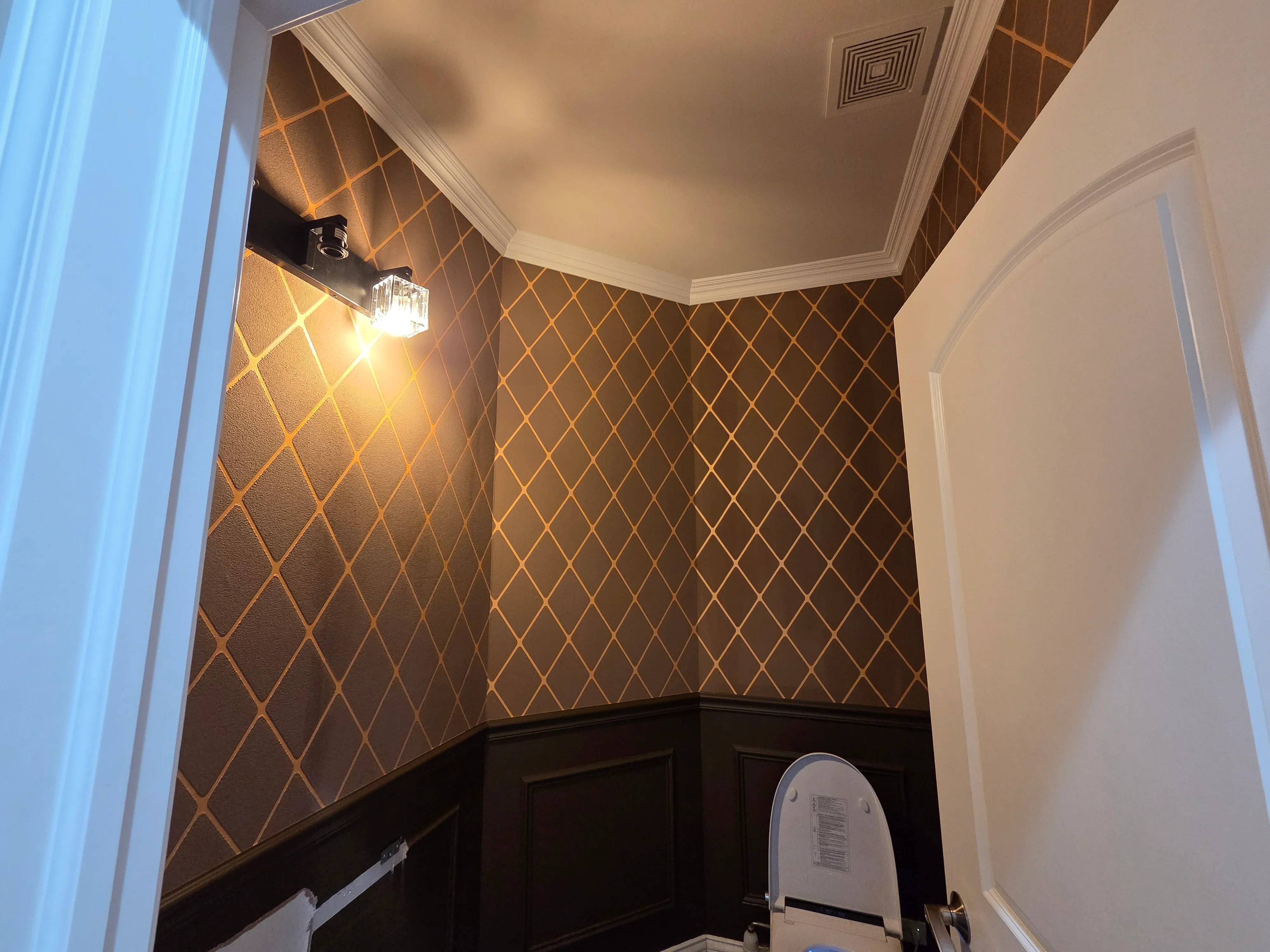 Charcoal and gold geometric wallpaper with black wainscoting and white crown molding in powder room