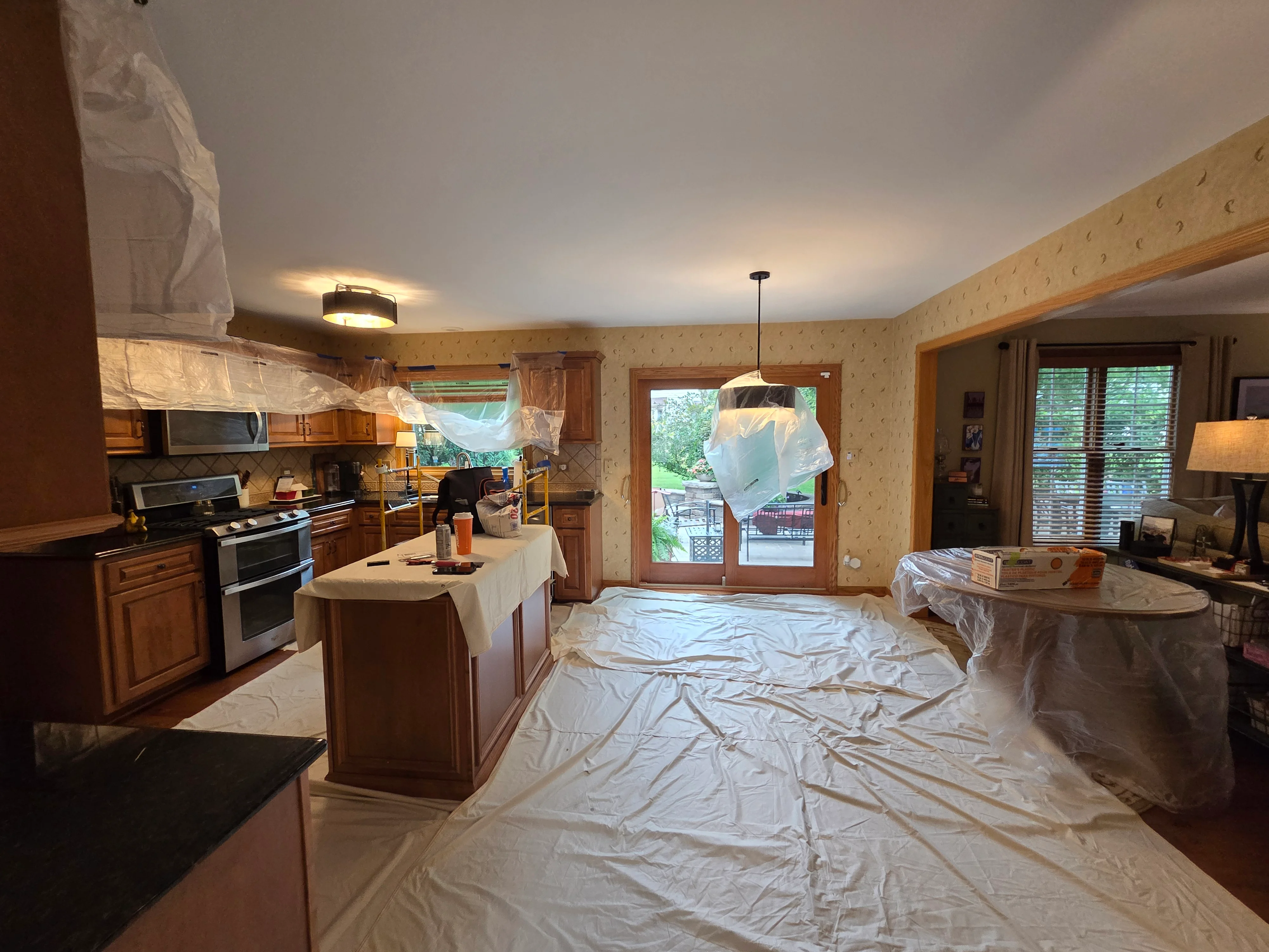 Kitchen interior with wood cabinets, protective plastic sheeting, and ceiling painting in progress